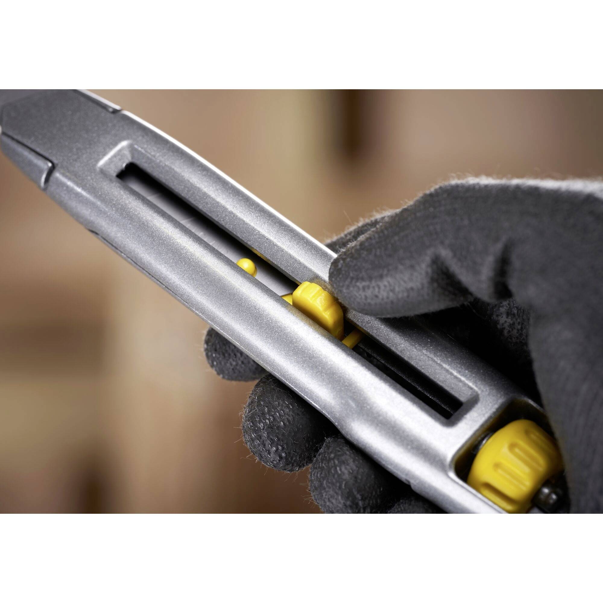 A hand protected by a black glove operates a silver cutter with yellow details, sliding the blade forwards.