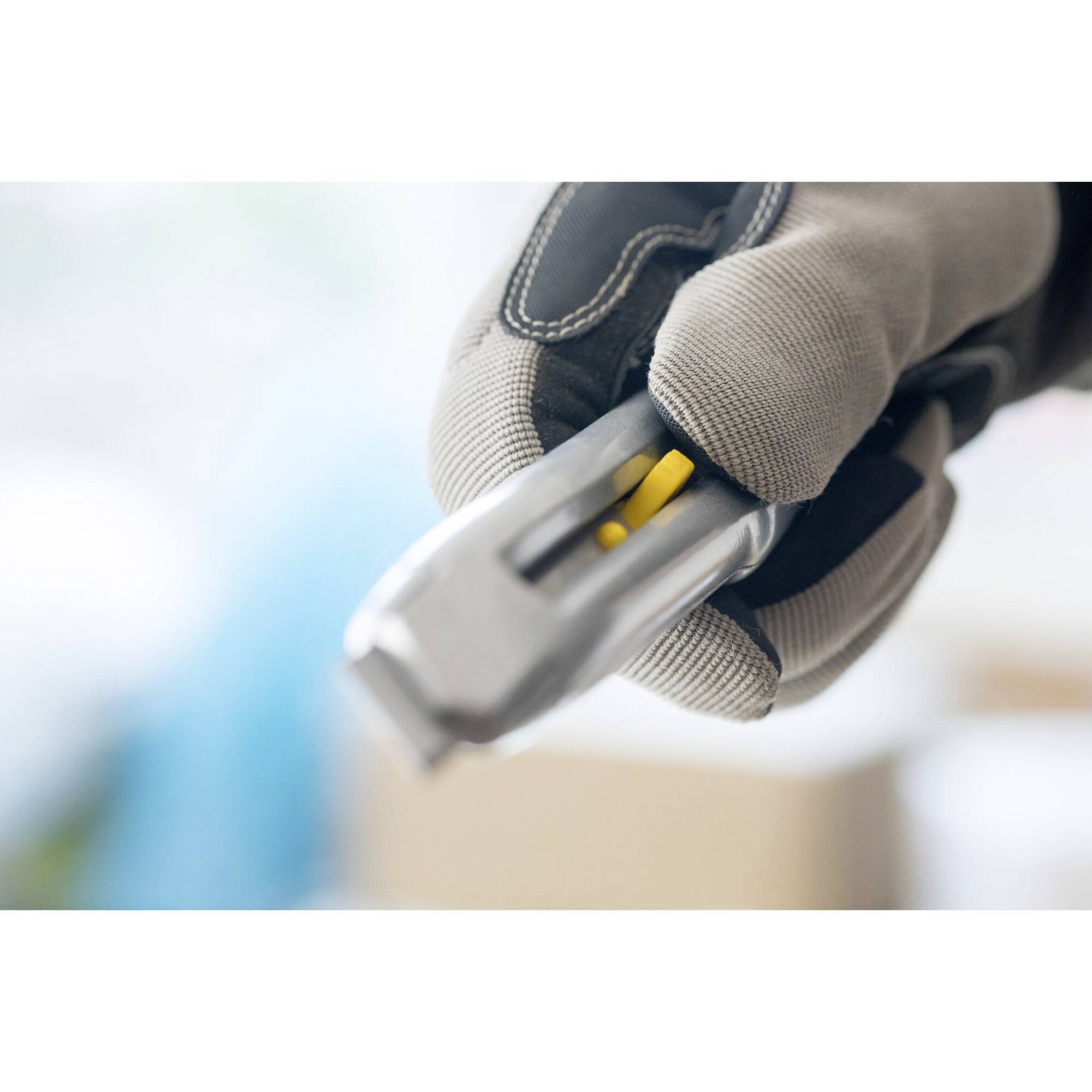 A hand holds a bicycle tool in close-up, showing a yellow component. The person is wearing protective gloves.