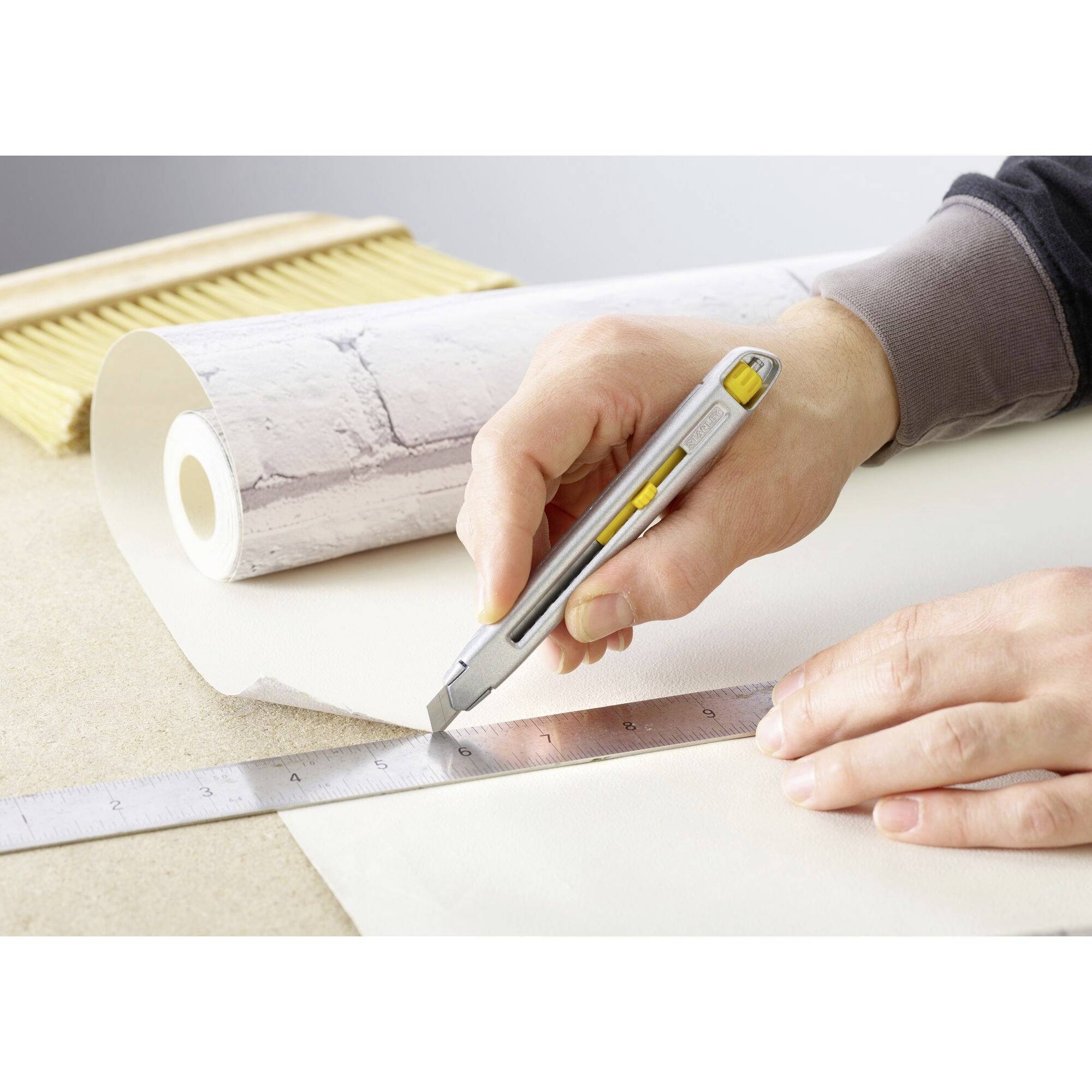 A person is cutting wallpaper along a ruler using a craft knife.