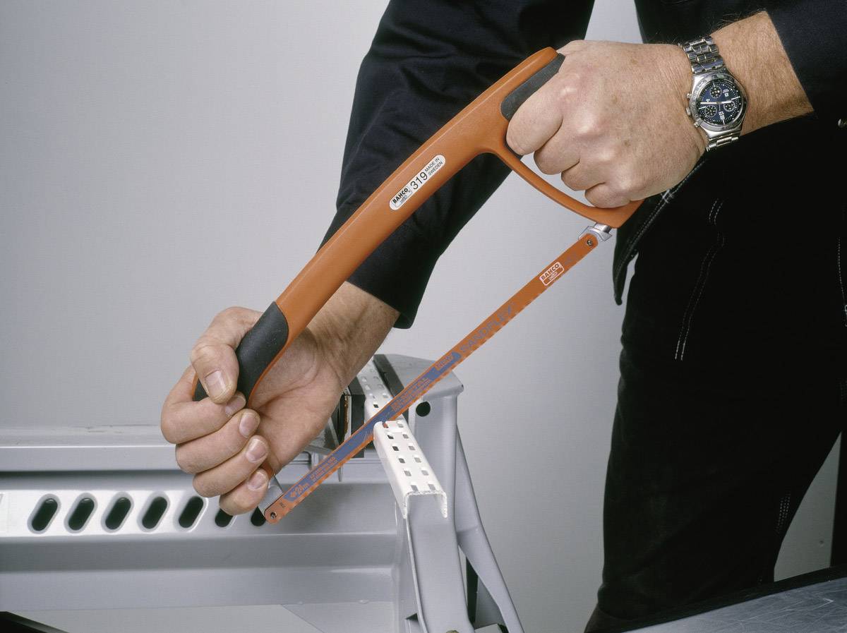Eine Person sägt mit einer Bügelsäge durch ein Metallrohr, das an einem Tisch festgeklemmt ist.