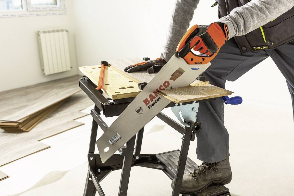 Eine Person sägt mit einer Handsäge ein Holzstück auf einer Werkbank. Im Hintergrund sind Laminatdielen zu sehen.