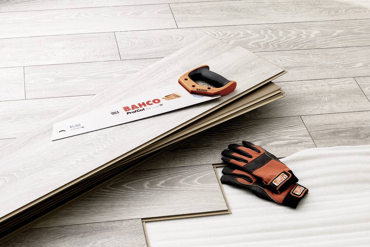 Eine Säge und Arbeitshandschuhe liegen auf hellem Laminatboden neben unmontierten Bodenplatten, die für Renovierungsarbeiten vorbereitet werden.