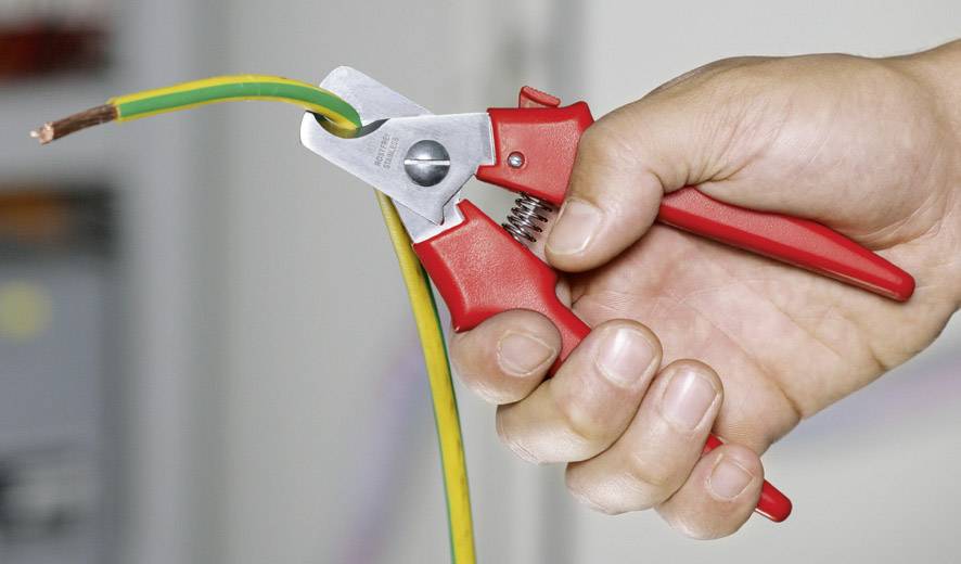 A hand is holding a red wire stripping plier and removing the insulation from a green and yellow electrical cable.