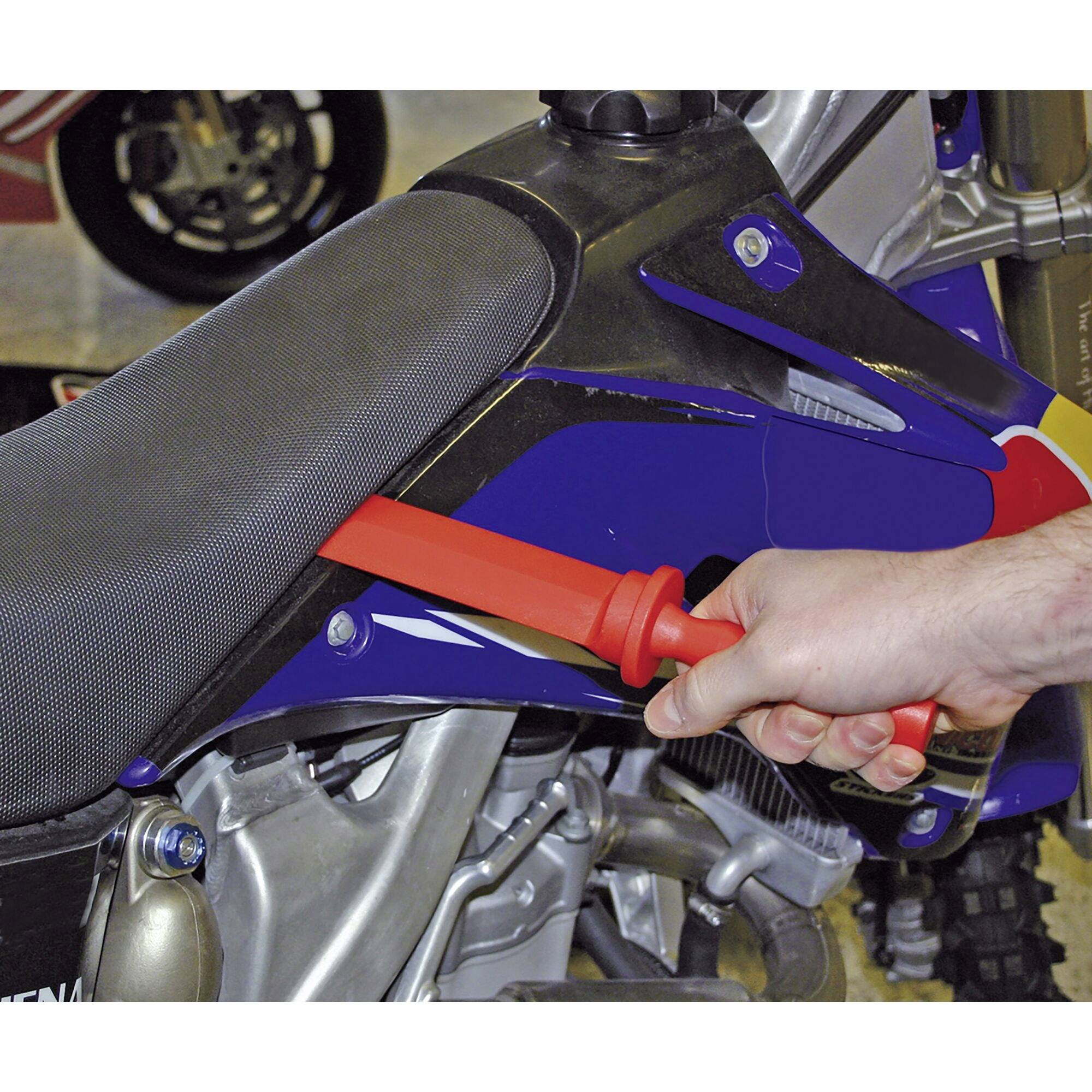 A person is checking the tyre pressure of a motorcycle with a red pressure gauge. The motorcycle has a blue fairing.