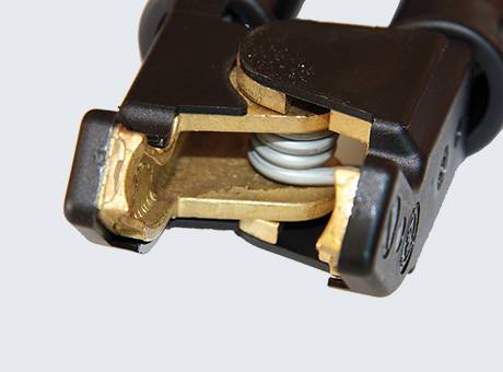 Close-up of a brass electrical clamp with a visible spring mechanism, used for secure connections in battery terminals.