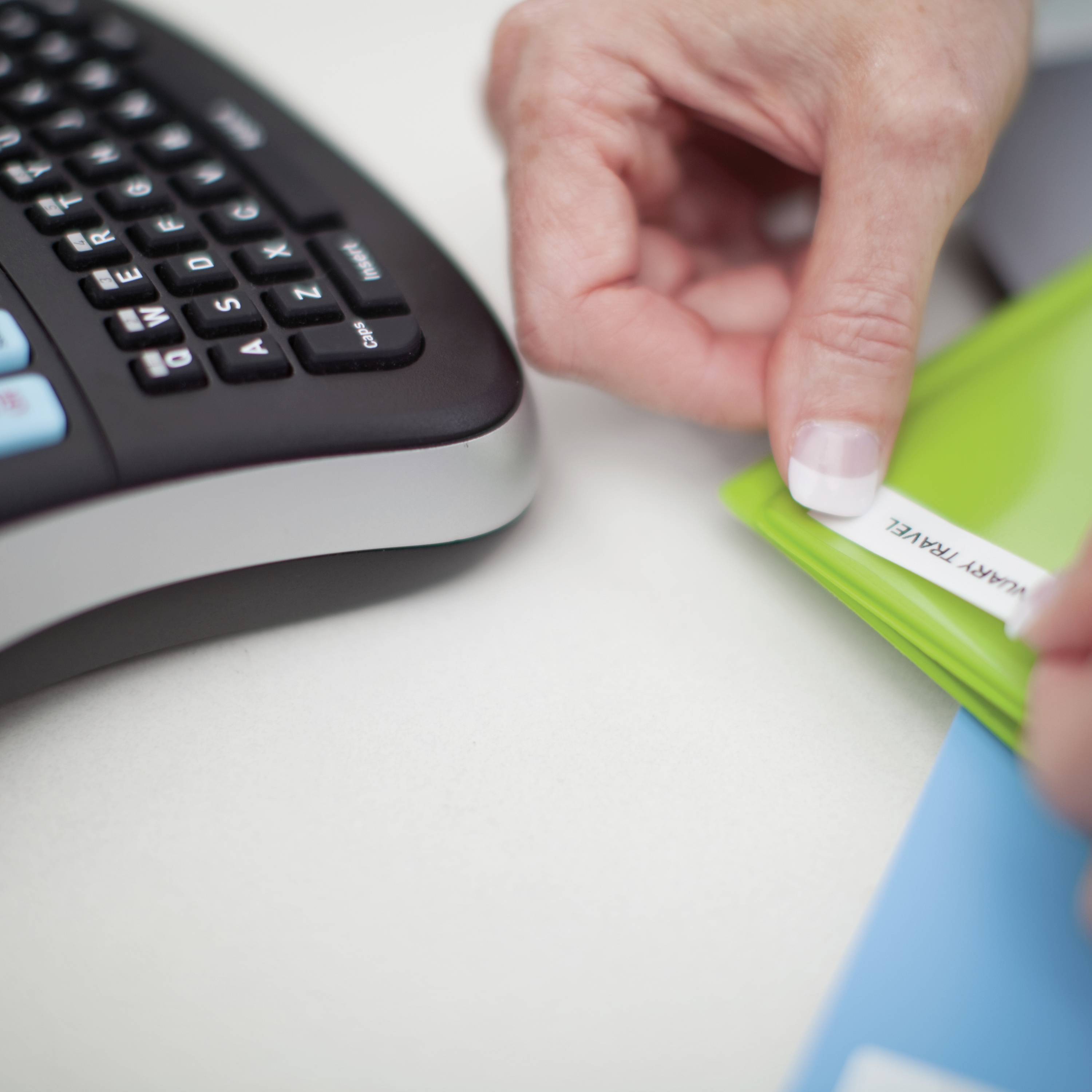 A hand places a label reading 'IMPORTANT FILE' into a green folder next to a computer keyboard on a desk.