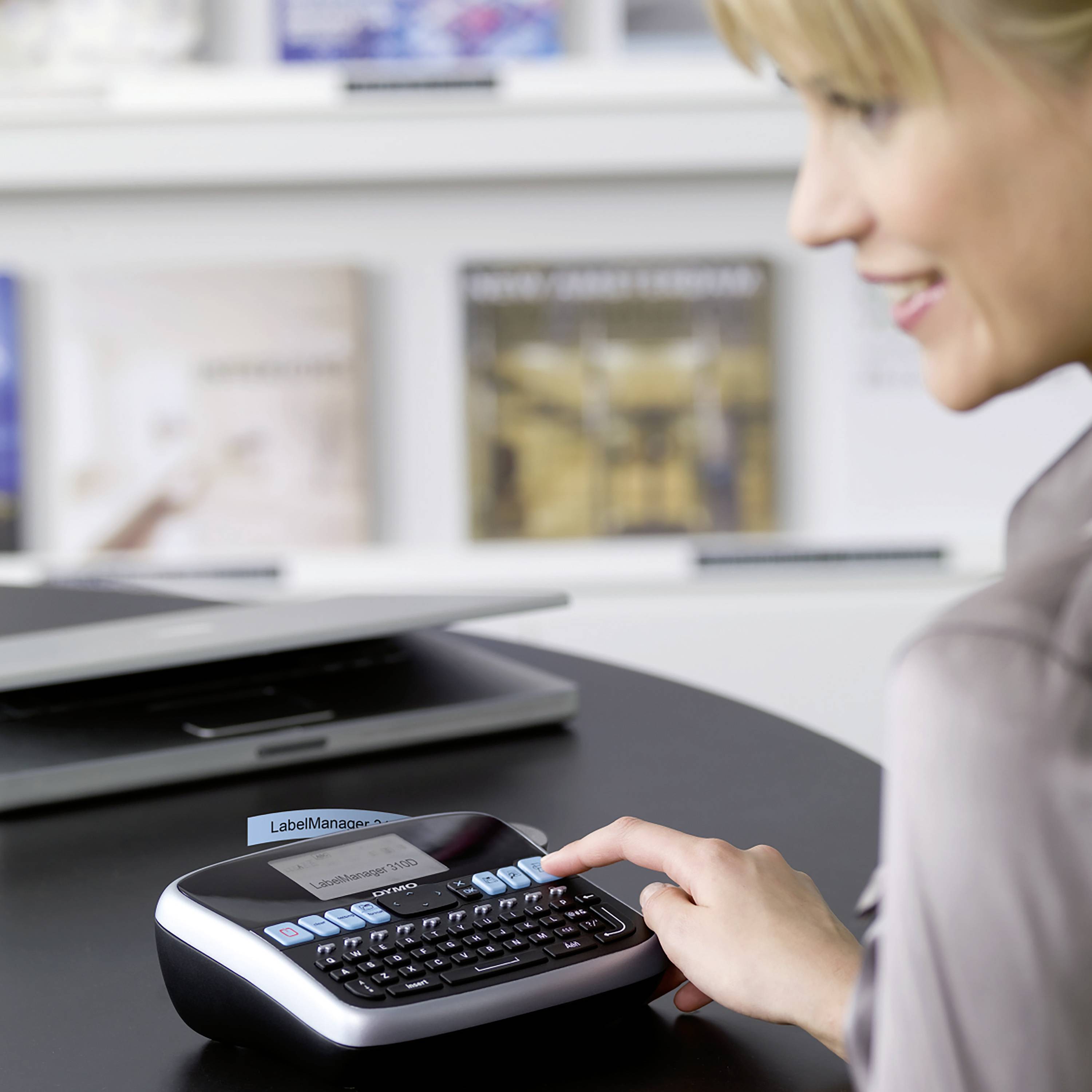 A person is using a label maker to print a label with the inscription 'LabelManager'. A table is visible in the background.