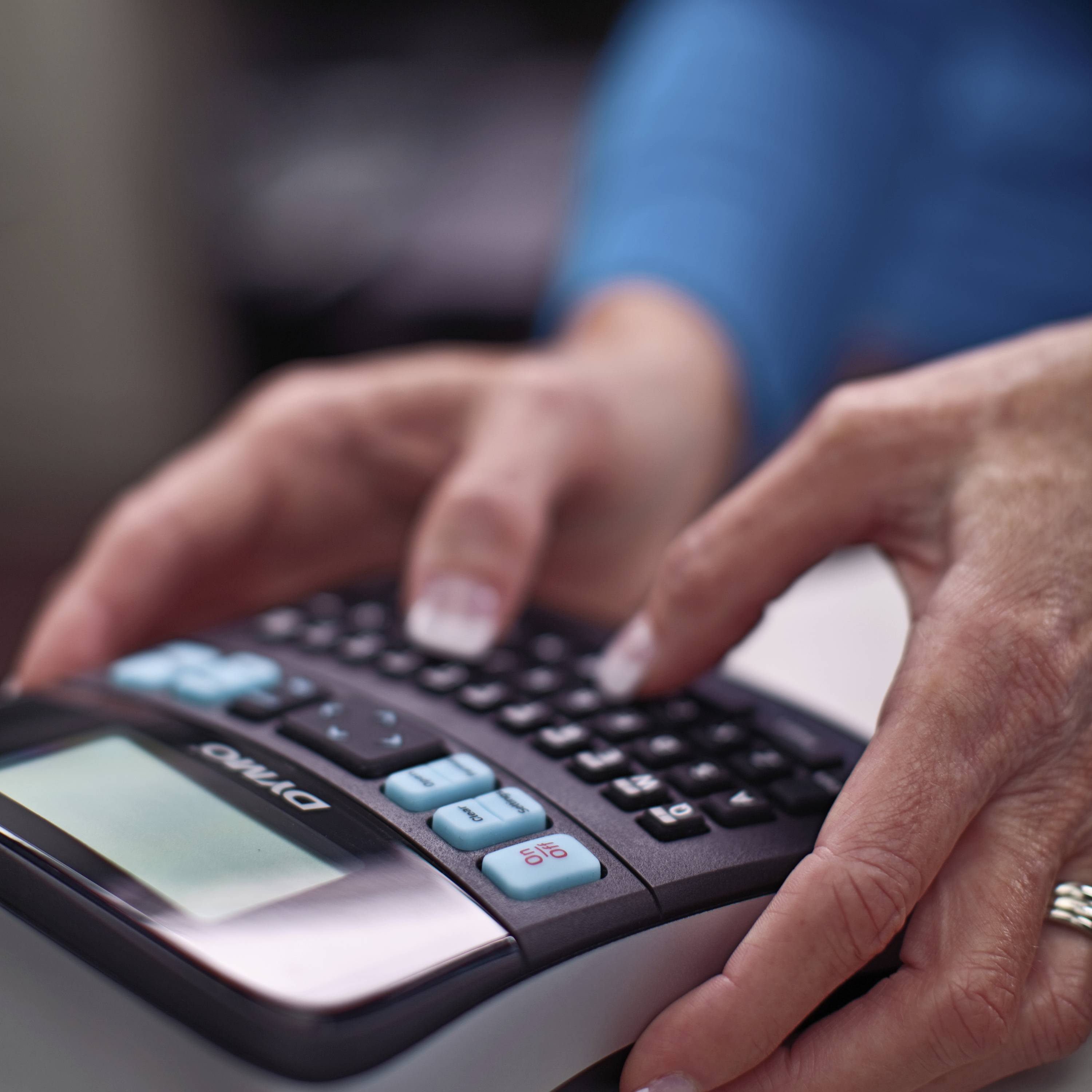 A person is typing on a calculator. The focus is on their hands as they press the buttons.