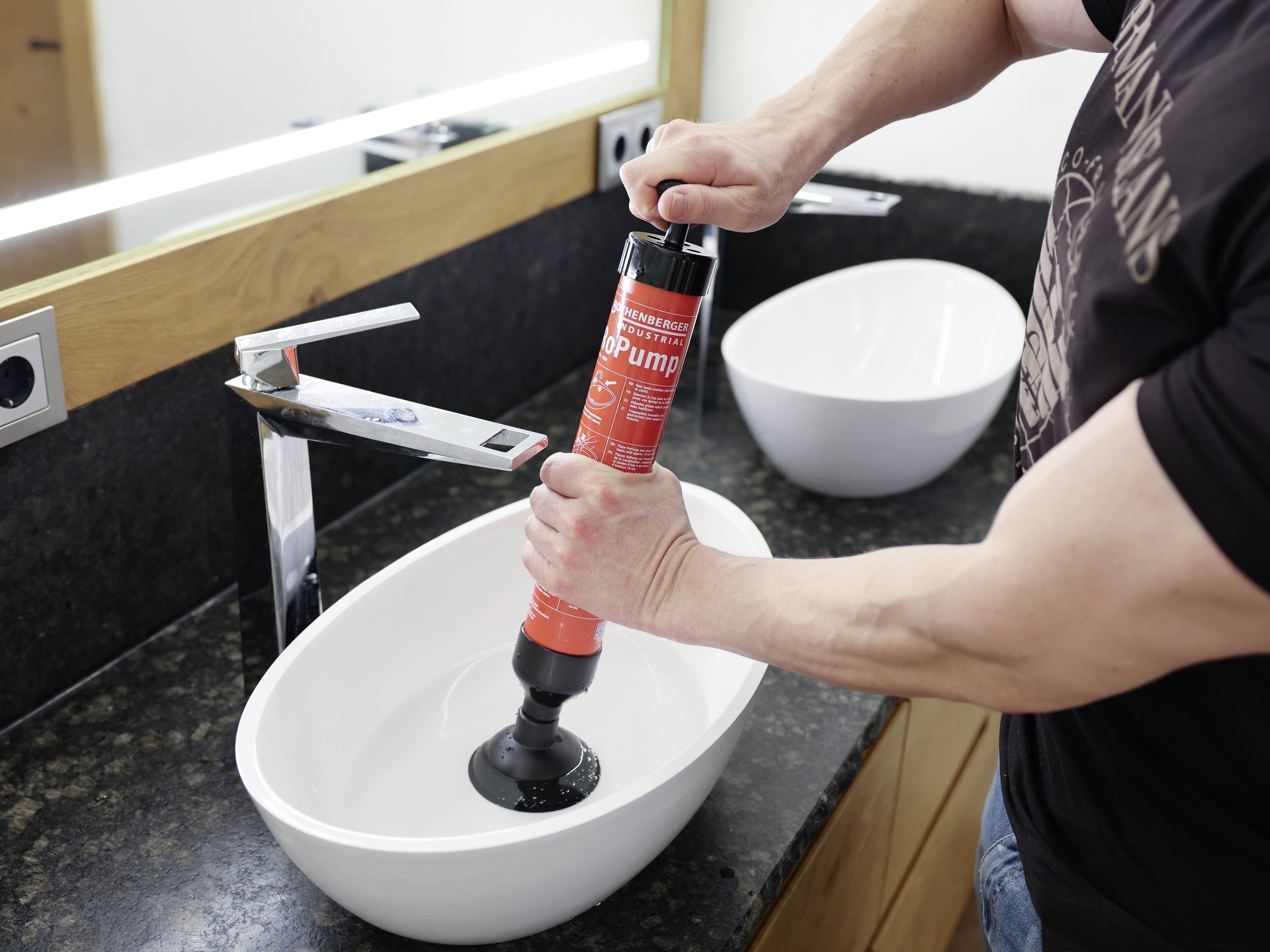 A person is using a plunger in a sink in the bathroom to clear a blockage.