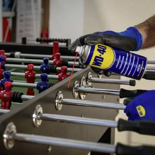 A person is spraying lubricant onto the rod of a table football game to improve the movement of the figures.