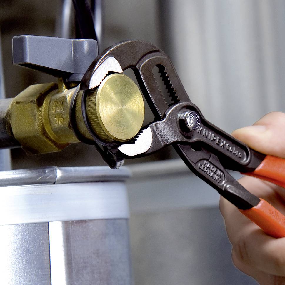 A hand is using a pipe wrench to tighten a brass nut on a water connection.