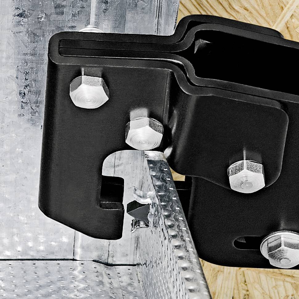 A black metal bracket, secured with several bolts to a silver, ribbed surface.
