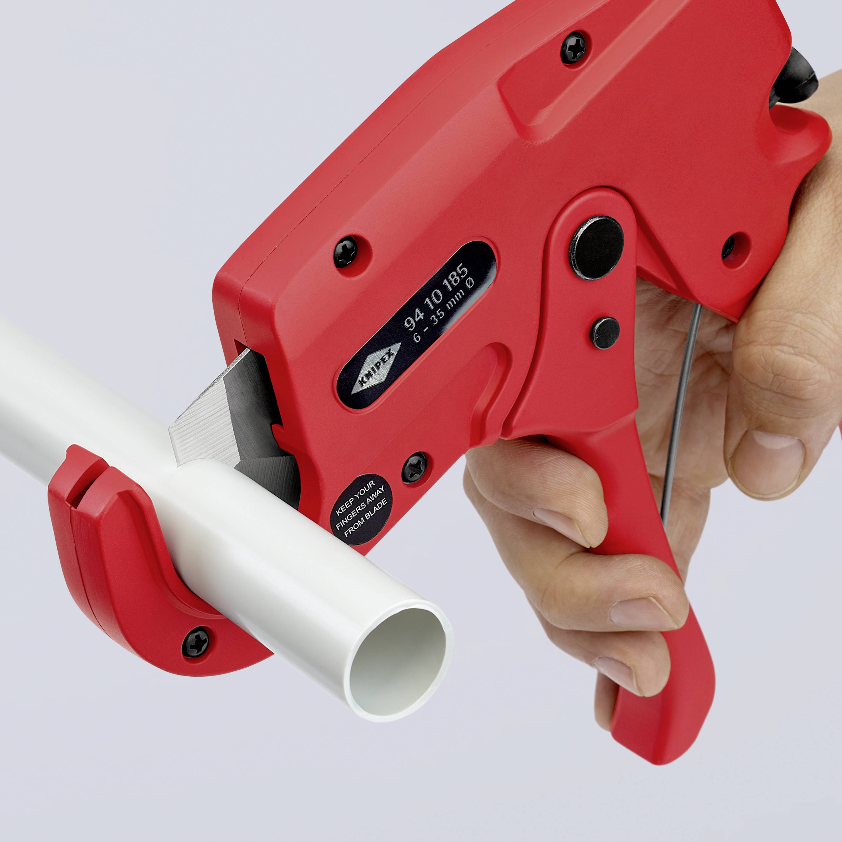 A person is cutting a white pipe with a red pipe cutter. The focus is on the tool and the cutting process.
