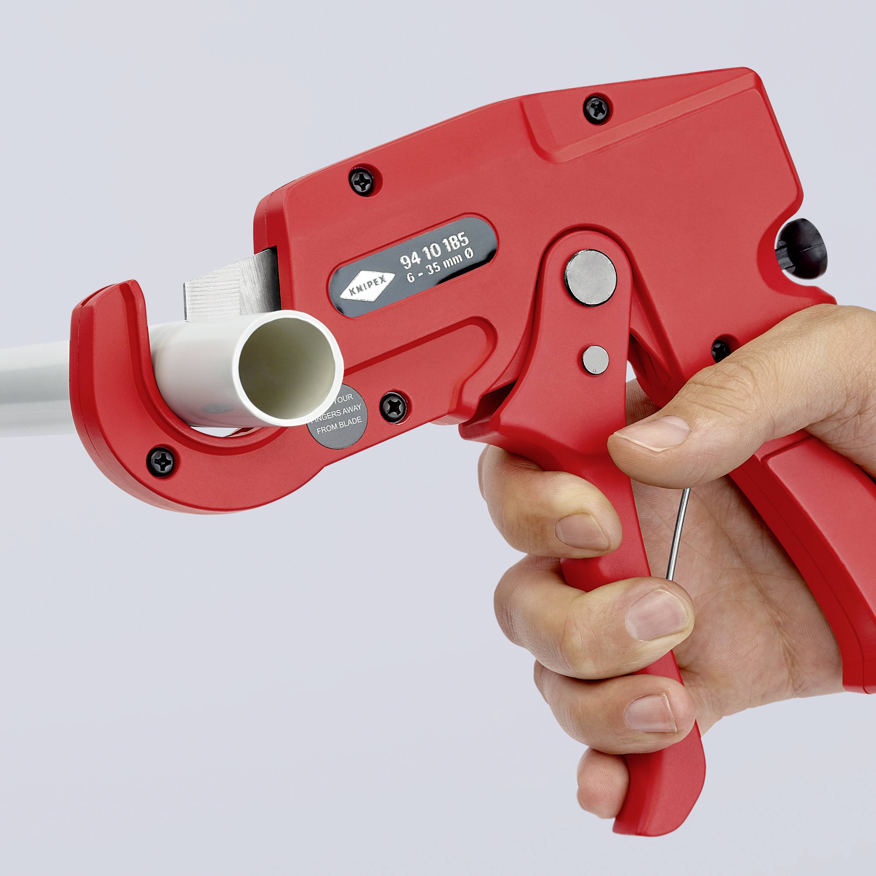A red hand crimper crimping a white pipe. One hand holds the handle, while the other operates the tool.