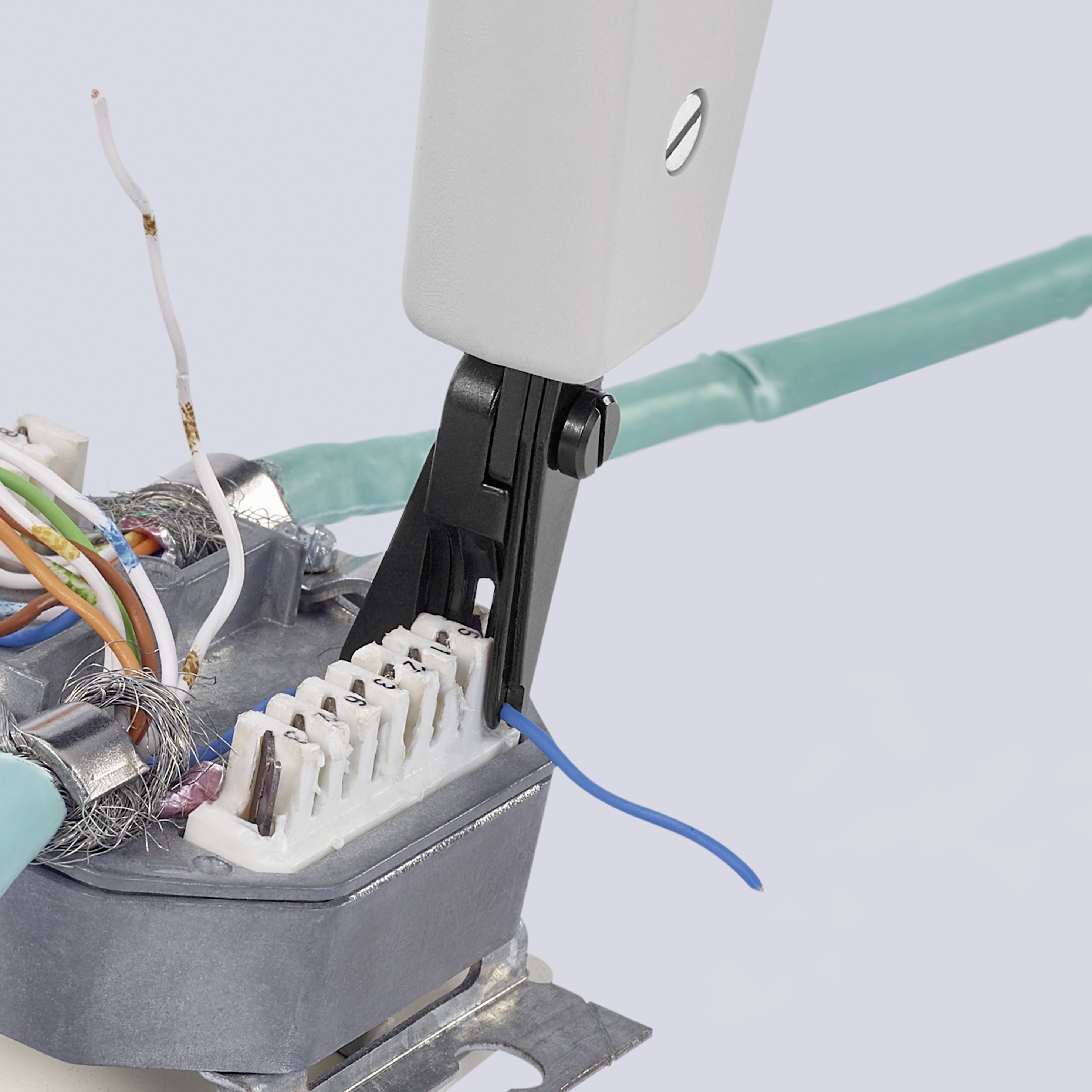 A pair of pliers clamps wires into an electrical connection module. Various cable ends are exposed and laid out side by side.