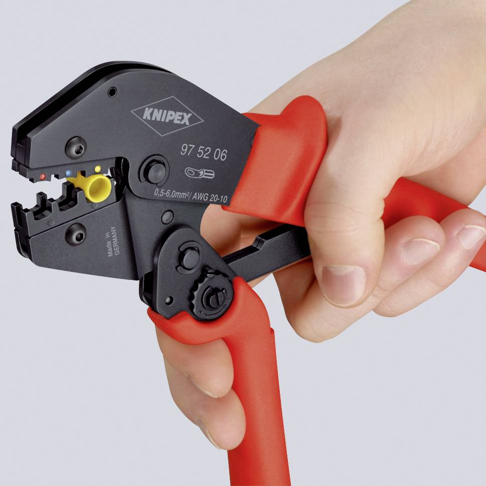 A hand is holding a red crimping pliers for stripping and crimping cables. The pliers have an adjustable crimping tool.