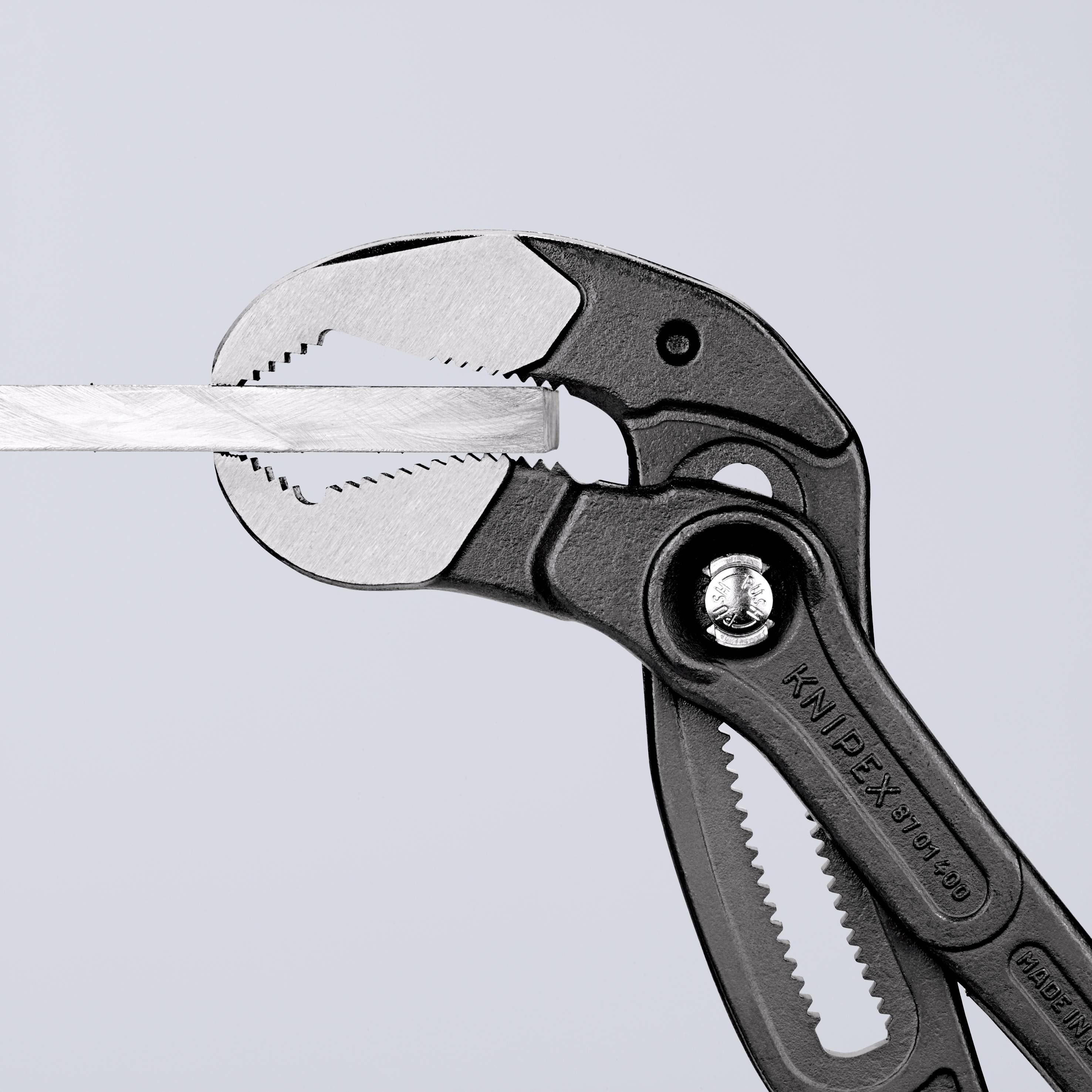 A pair of pliers grips a flat piece of metal. They are black with riveted joints. The brand name and model number are visible.