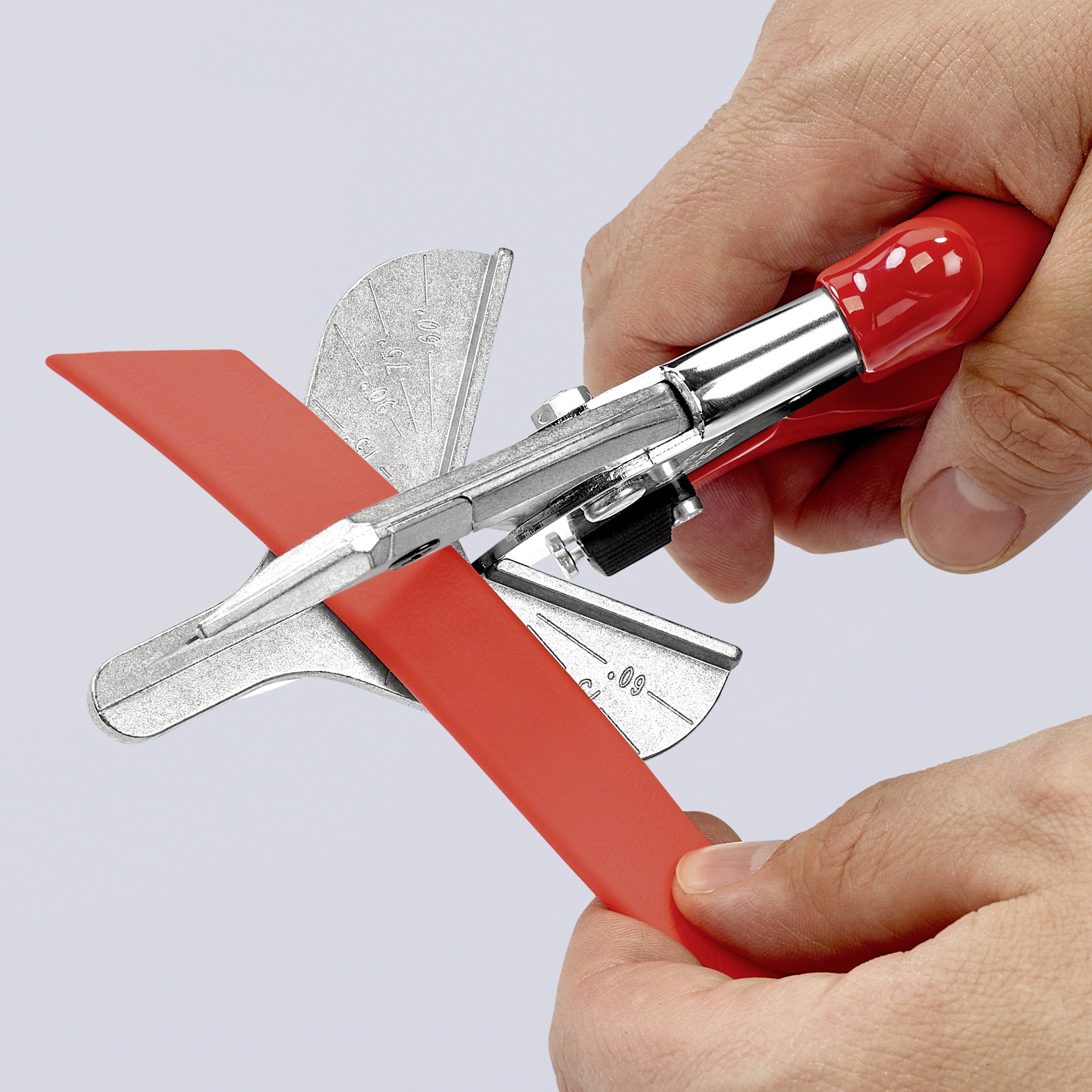 A hand is using a red, manual cutting tool to trim a piece of red plastic.