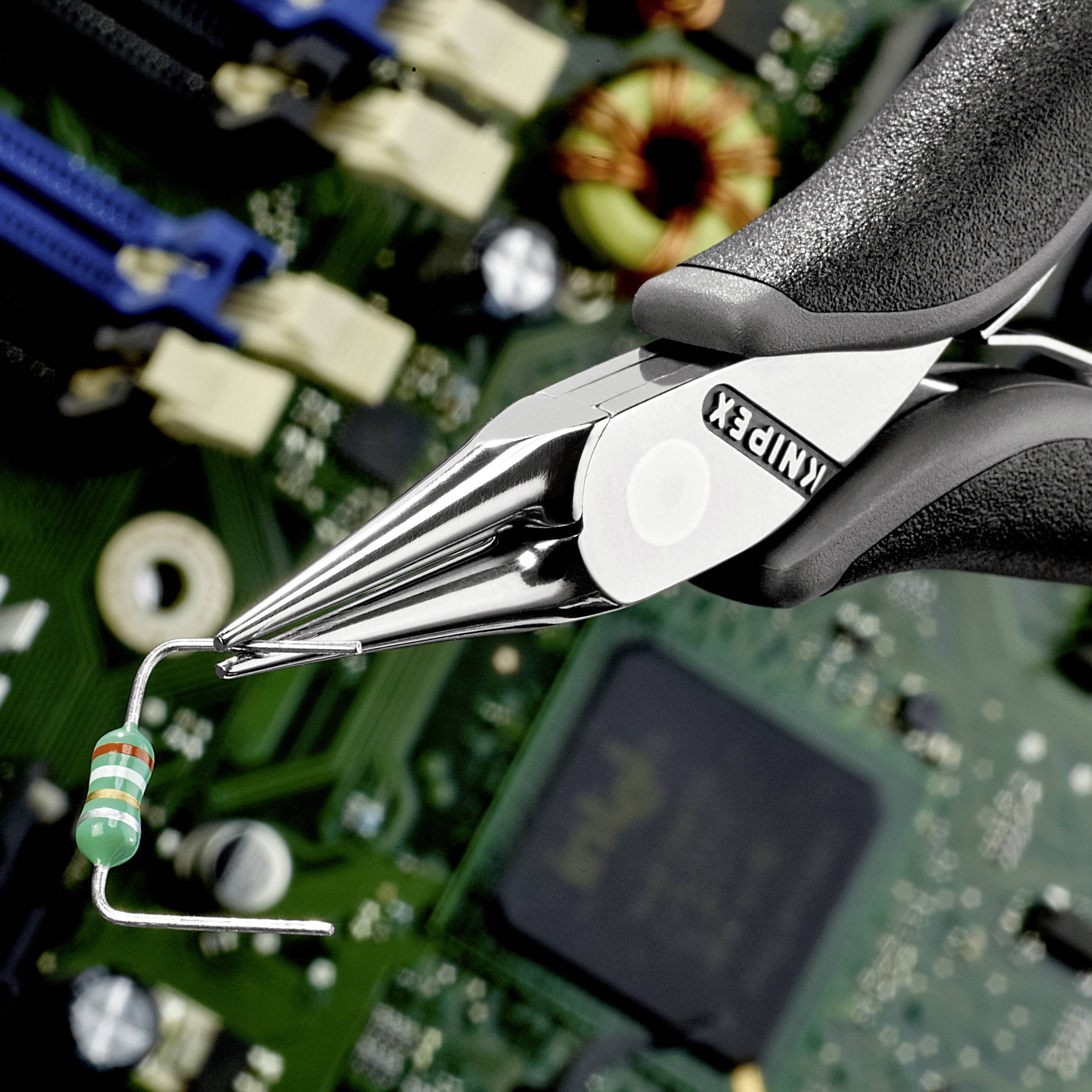 A pair of pliers holds a resistor over a circuit board. Electronic components can be seen in the background.