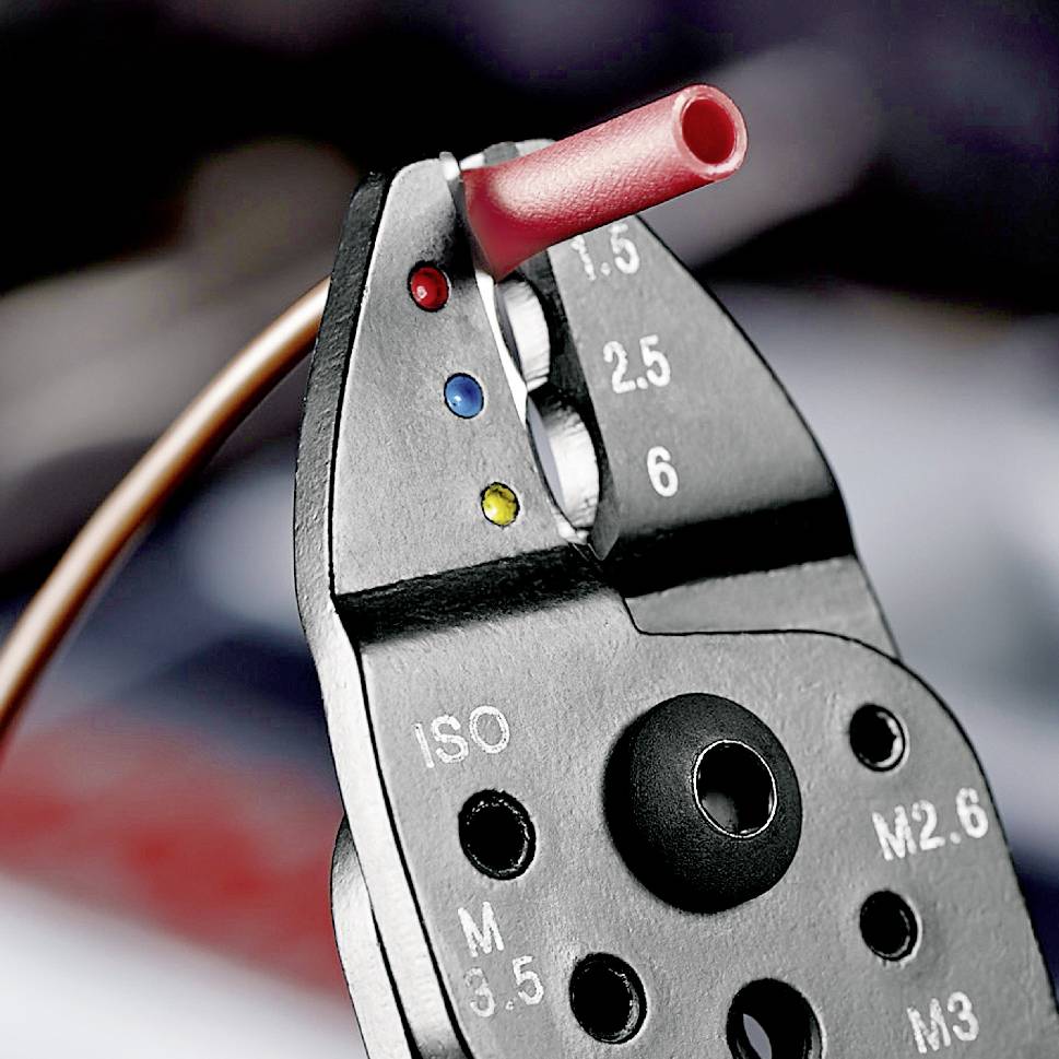 Close-up of a wire stripping tool with multi-coloured cutting slots for cable sizes, red insulation being cut.