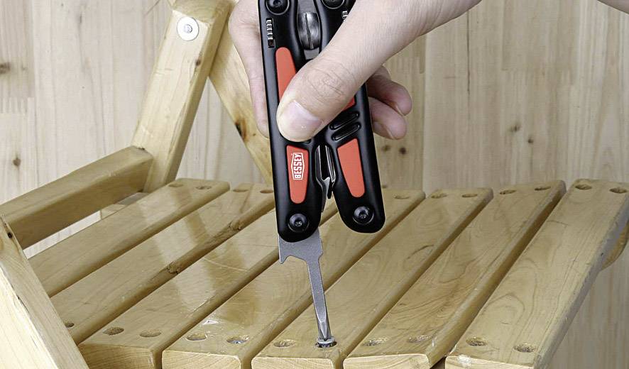 A hand is using a black and red multi-tool to tighten a screw in a wooden folding chair.