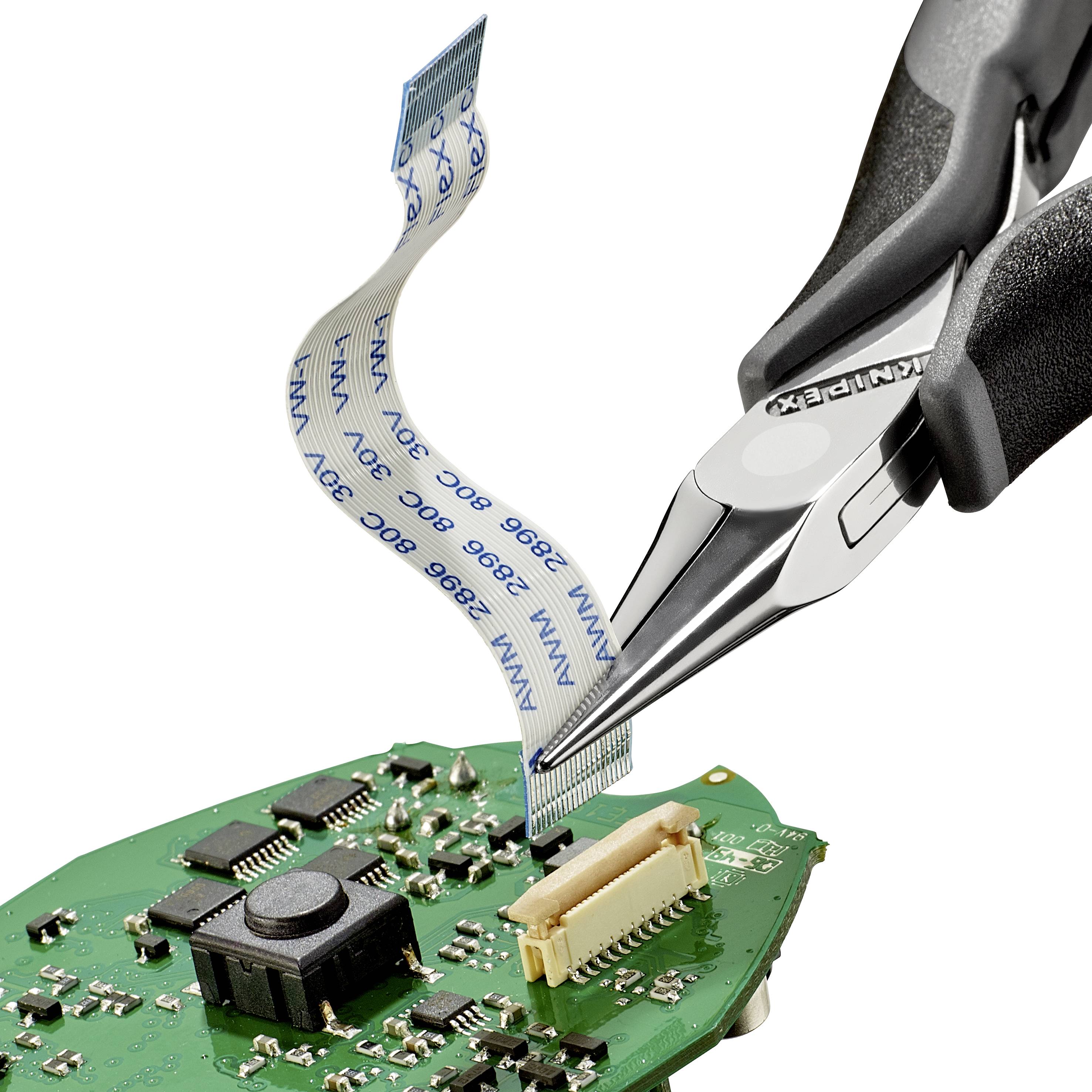 A pair of pliers is holding a flat ribbon cable over a green electronic circuit board with multiple chips and connectors.