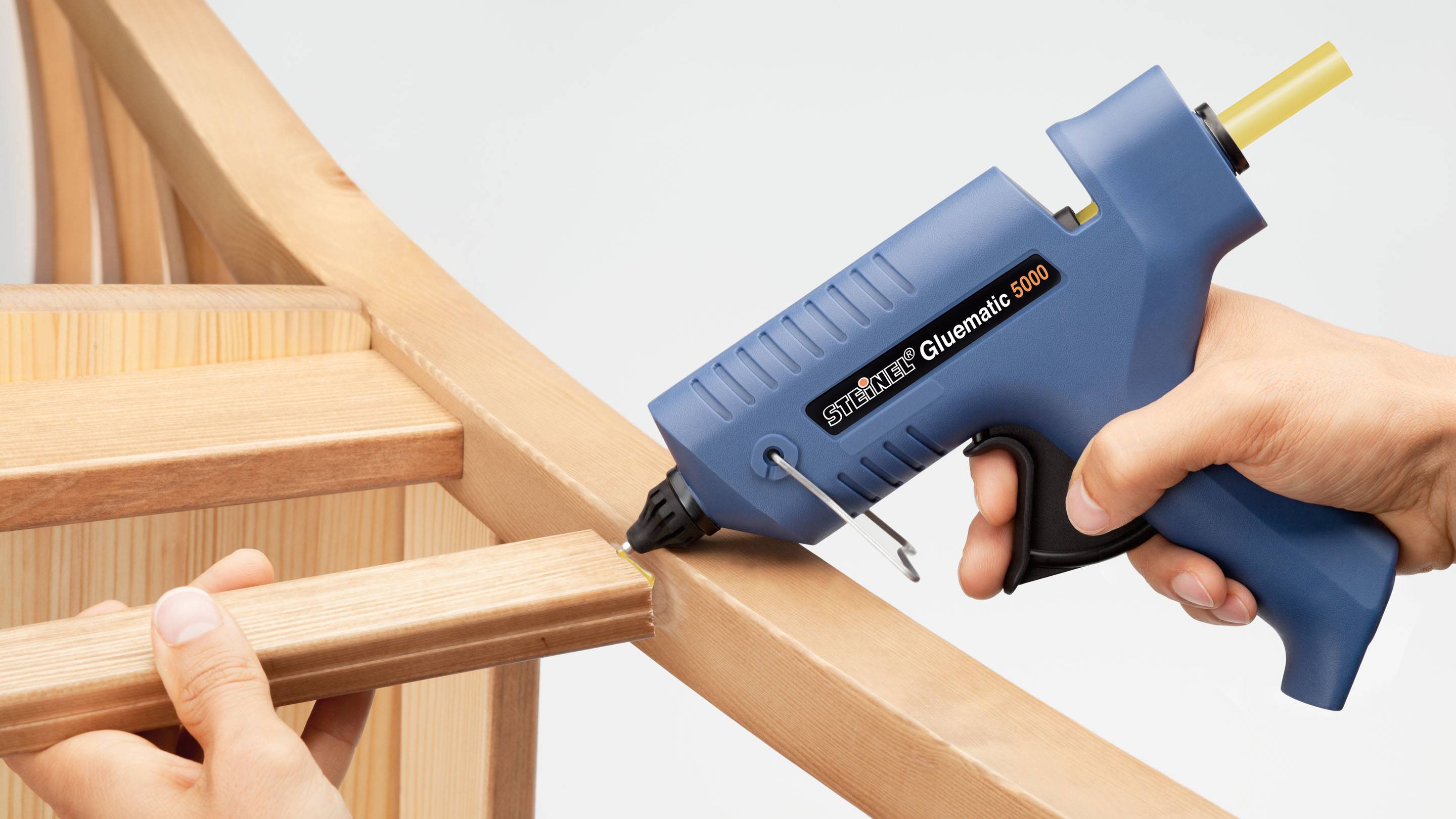 A person is using a blue hot glue gun to stick two pieces of wood together.