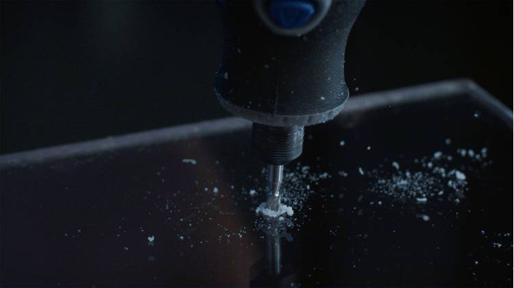 A close-up of a drill creating a hole in a dark surface, surrounded by debris.