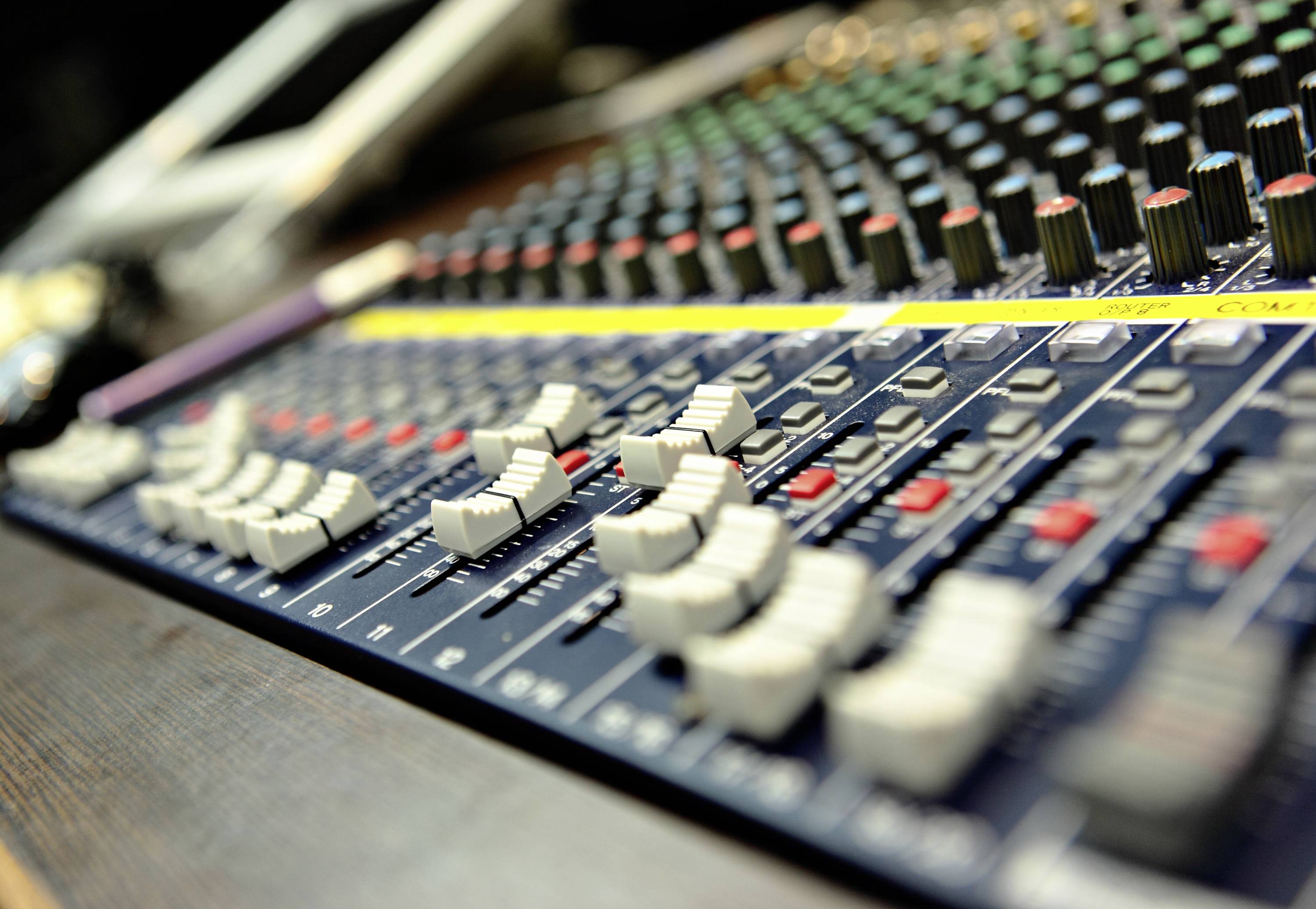Mixing desk with numerous sliders and rotary controls used for managing audio levels and tonal qualities in recording studios or at live events.