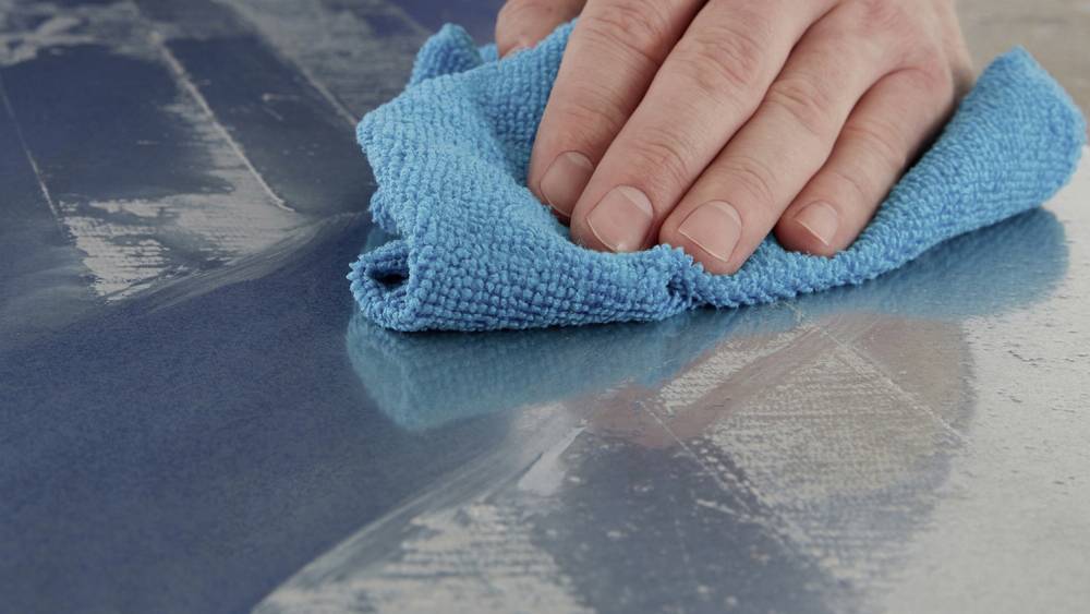 A hand wipes a wet surface clean with a blue microfibre cloth.
