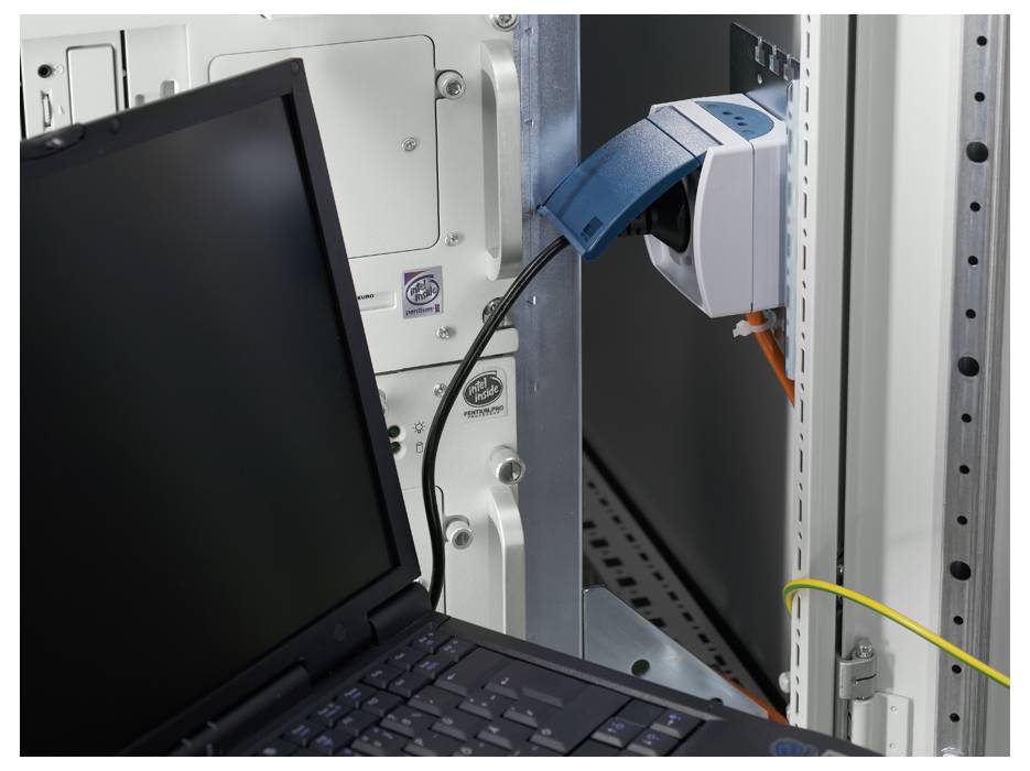A laptop is connected to a network cabinet. A network cable runs from the laptop to a socket in the cabinet.