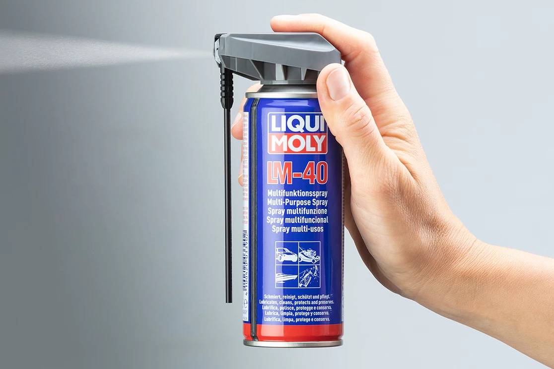 A hand is holding an aerosol can of 'Liqui Moly LM-40'. The can is being used; a fine spray mist is emerging.