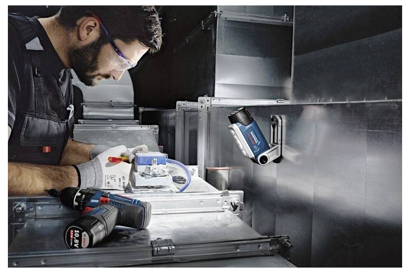 Technician wearing safety goggles and gloves, using a compact inspection camera on a metallic HVAC duct, focusing on controls.