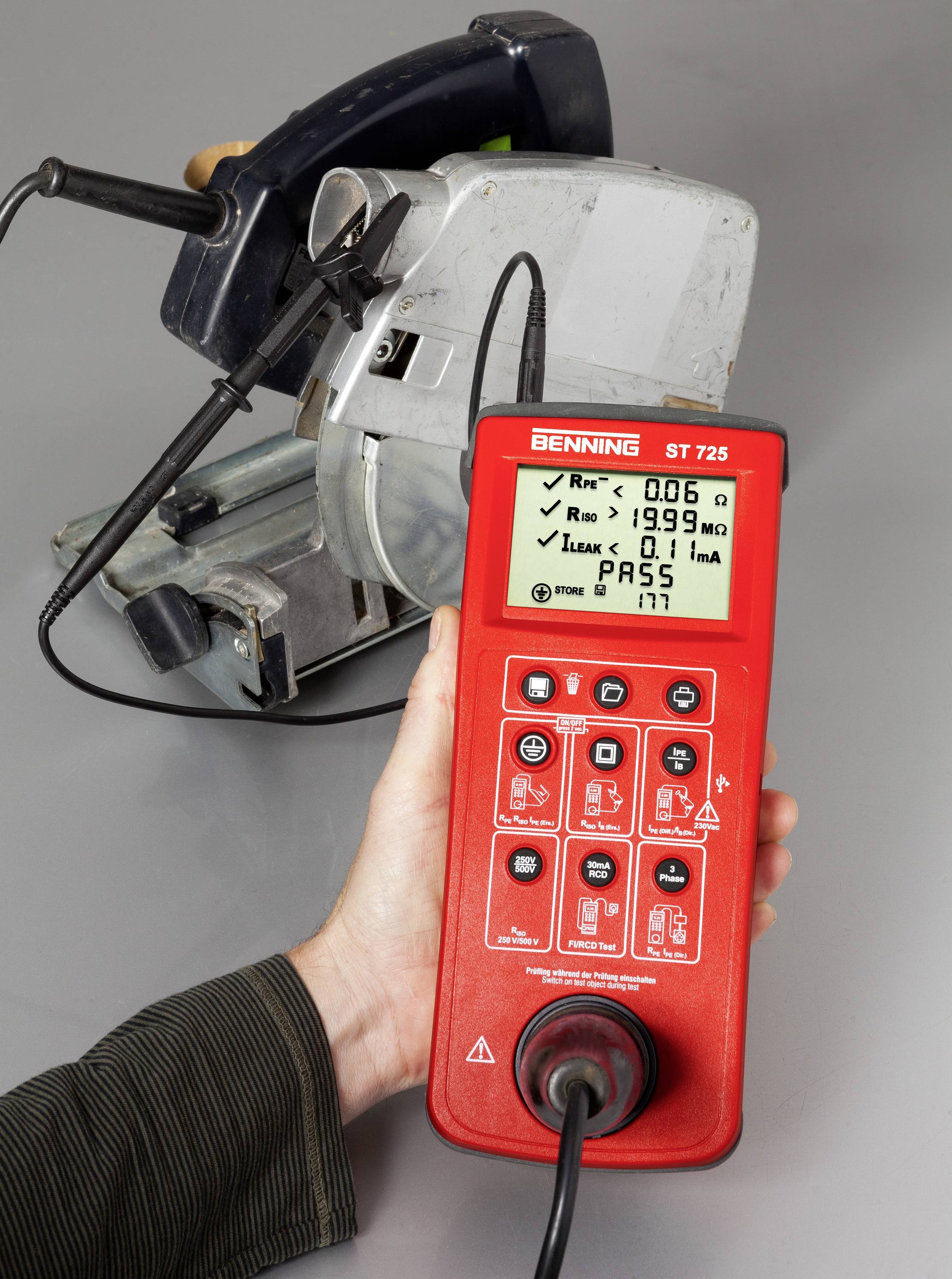 A person is testing an electrical machine using a Benning ST 725 testing device. The screen displays values and a 'PASS' indication.