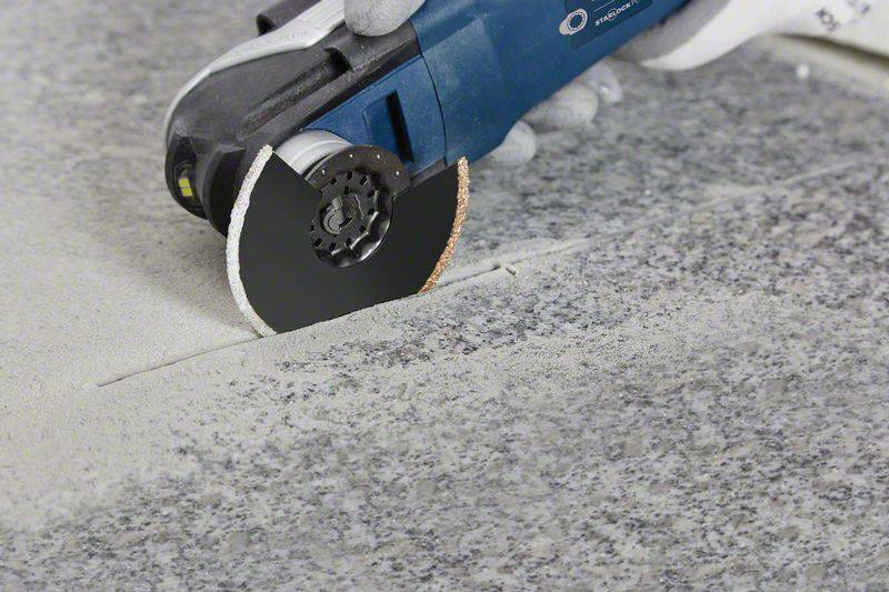 A person is cutting grey granite with a blue angle grinder. Dust is forming on the surface during the cutting process.