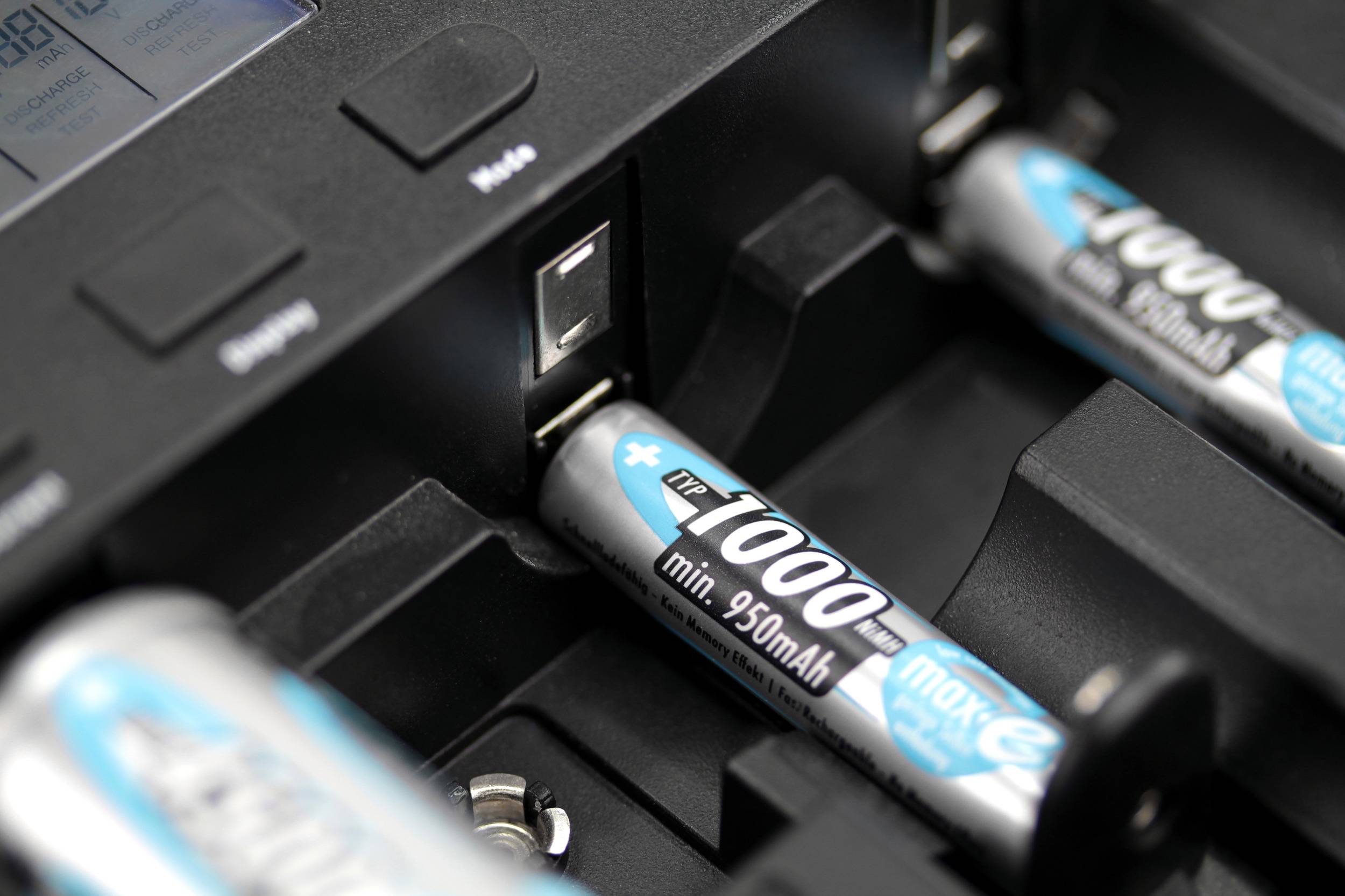 Close-up of a battery charger with AA rechargeable batteries inserted, being charged. The charging status is displayed on a screen.