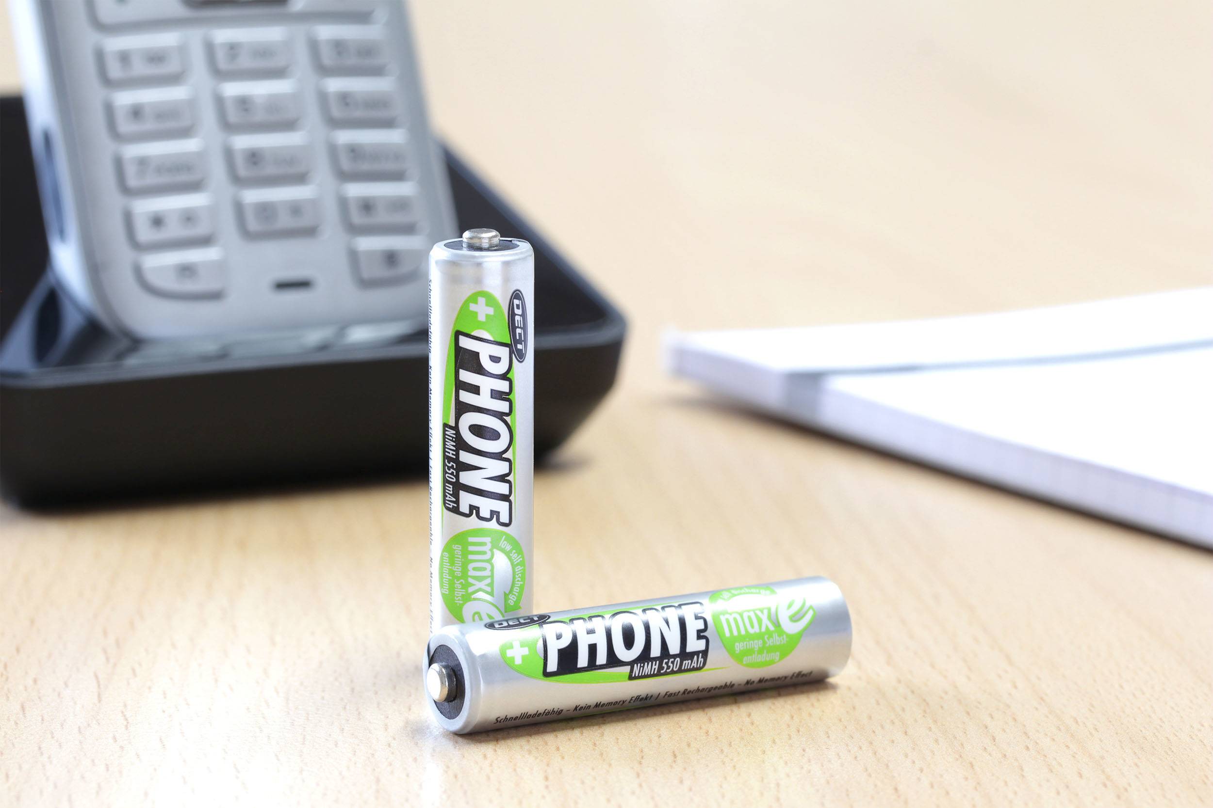 Two batteries sit in front of a cordless telephone on a table. A notepad lies in the background.