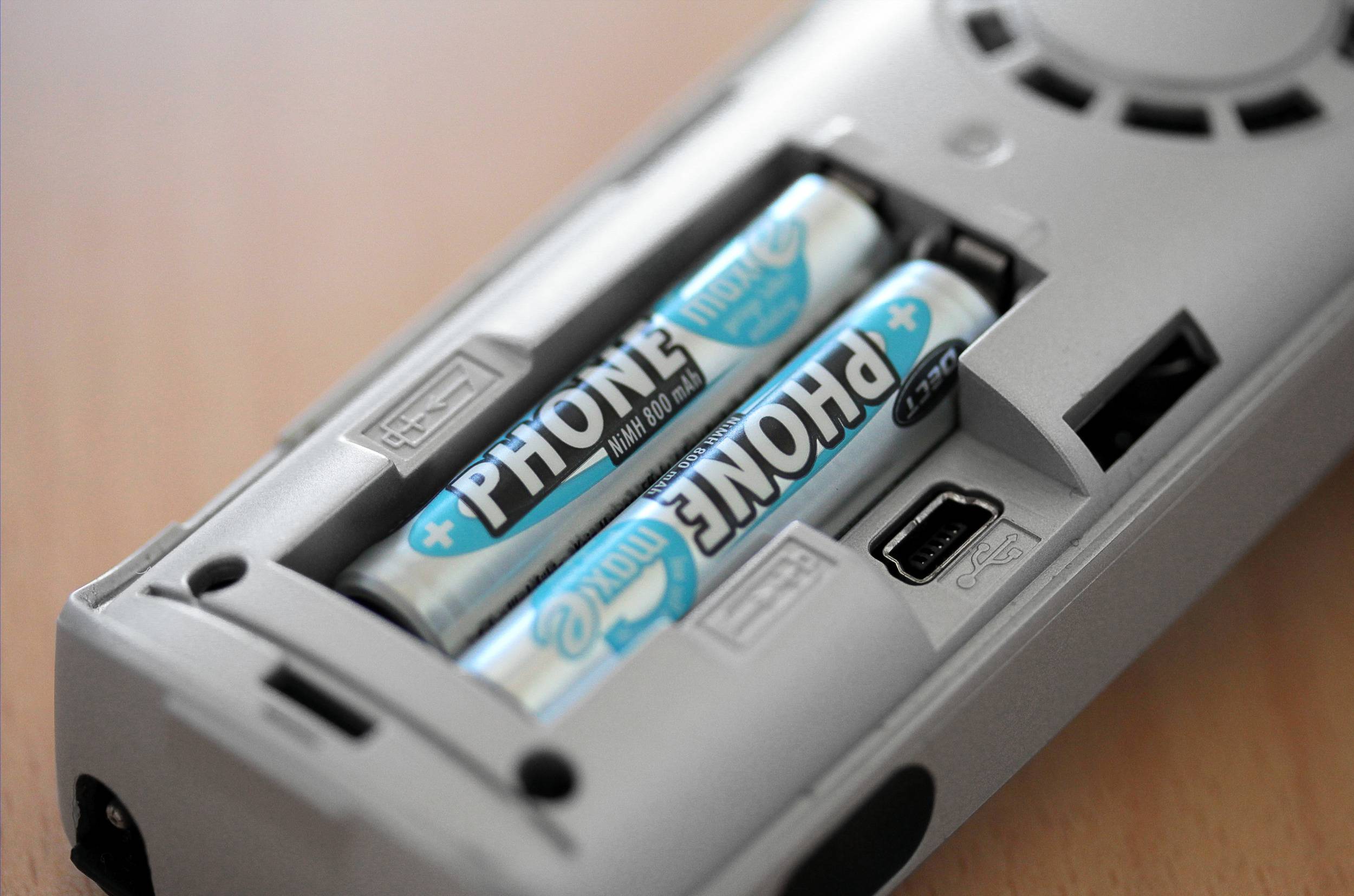 Two batteries in a grey remote control on a wooden table. The battery compartment is open and the batteries are visible.