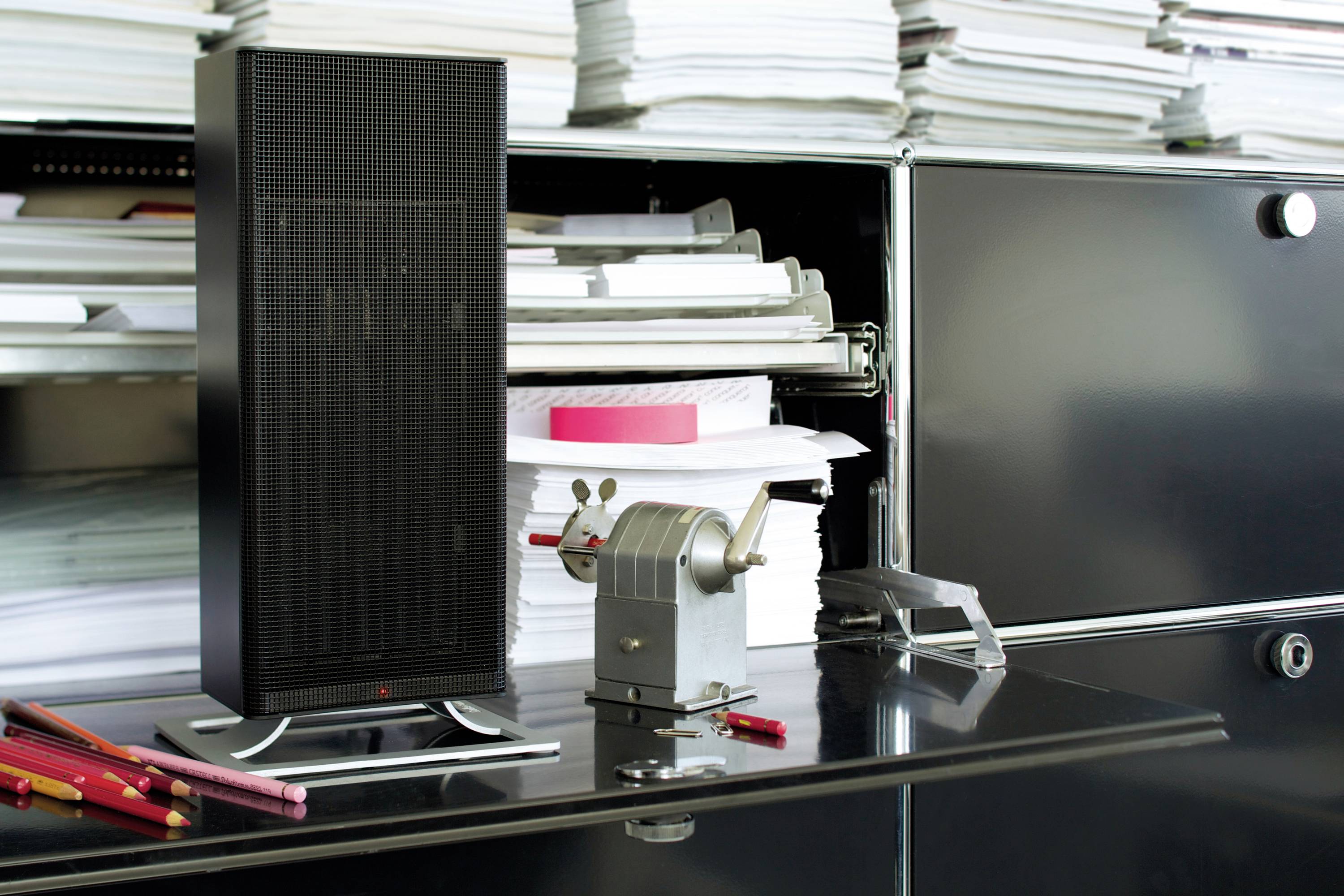Speakers, pencil sharpener and many files on a black desk. Office or work environment.