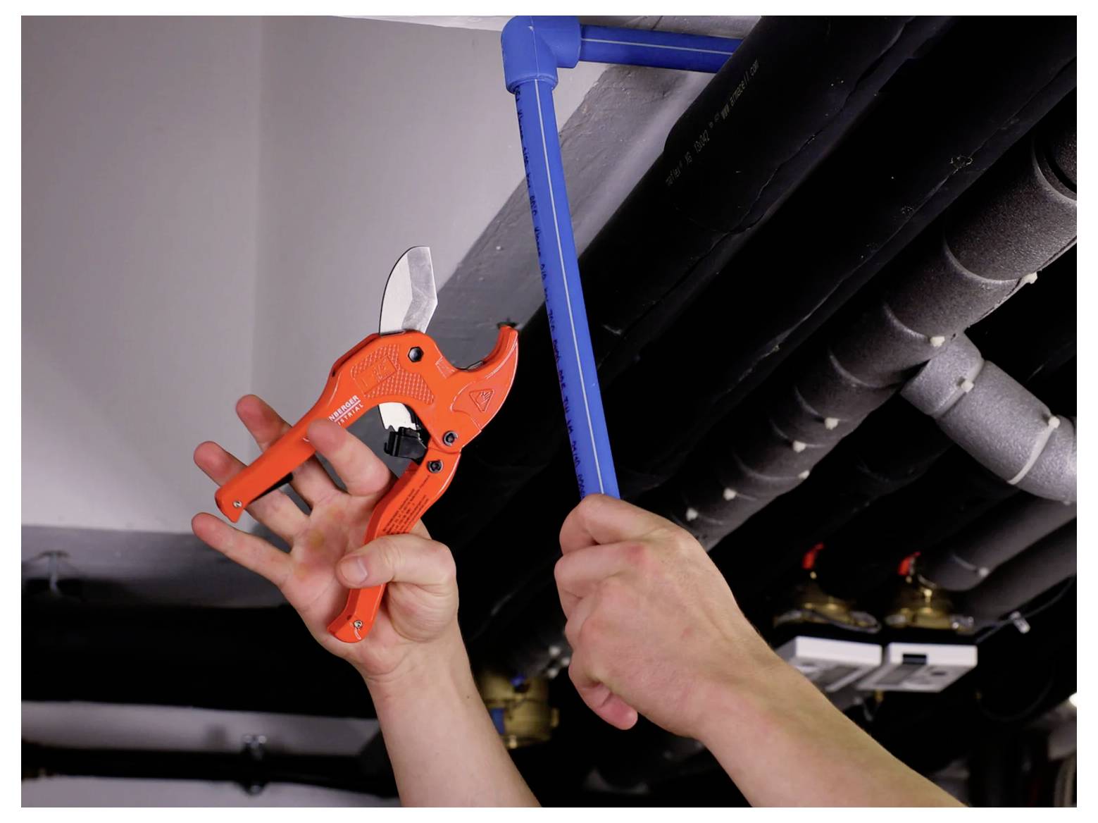 Person using a pipe cutter and blue support tool to work on overhead pipes in a ceiling space