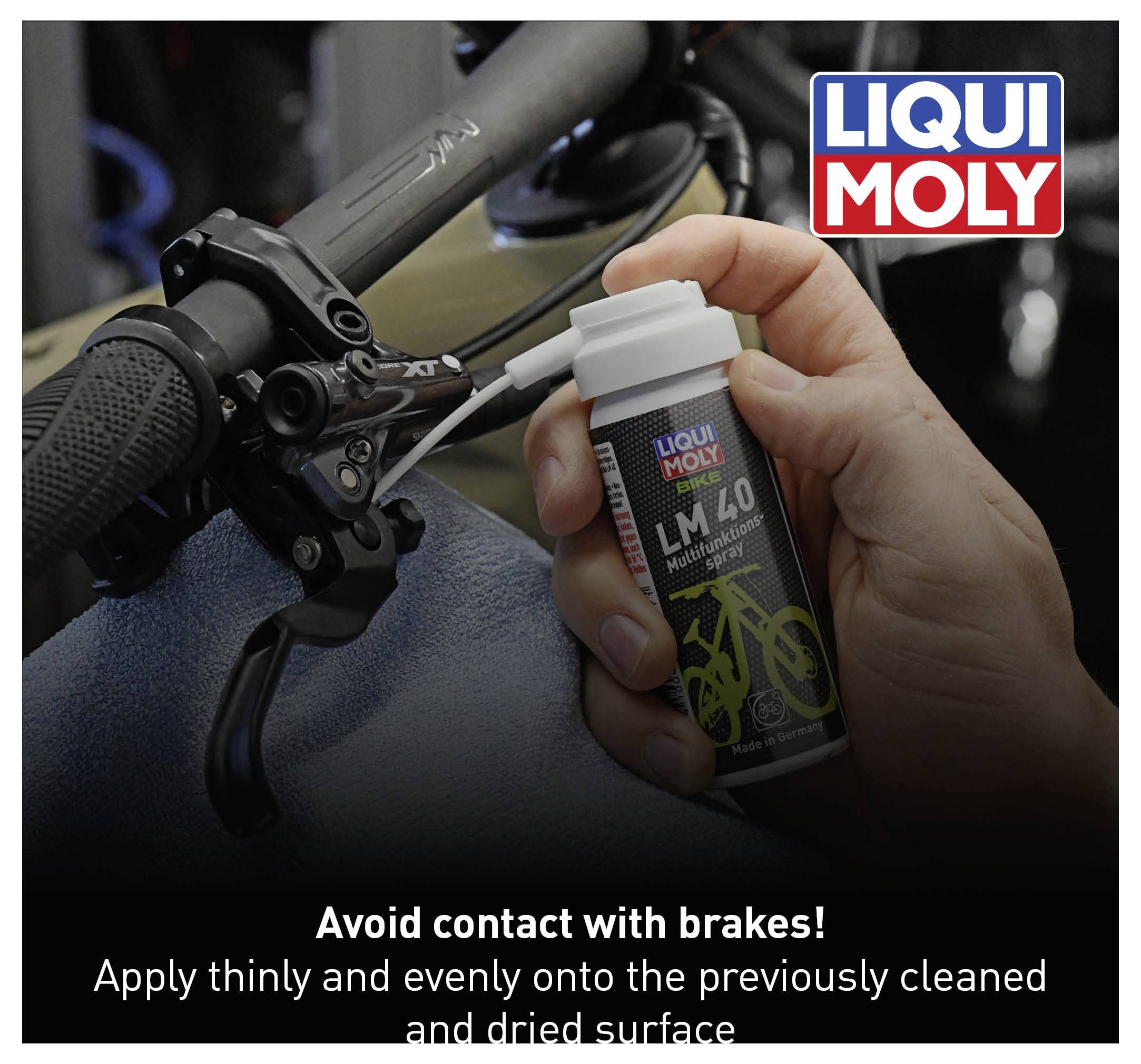 Bottle of Liqui Moly LM 40 being sprayed onto bicycle handlebars. Text: 'Avoid contact with brakes! Apply thinly to cleaned, dry surface.'