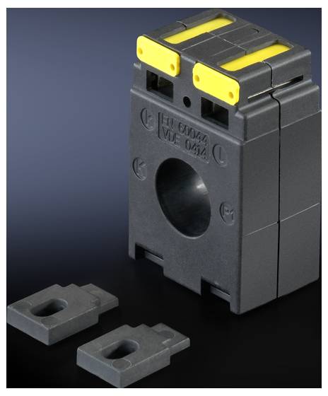 A black current transformer with yellow markings, alongside two rectangular accessory parts. The transformer has a central opening.
