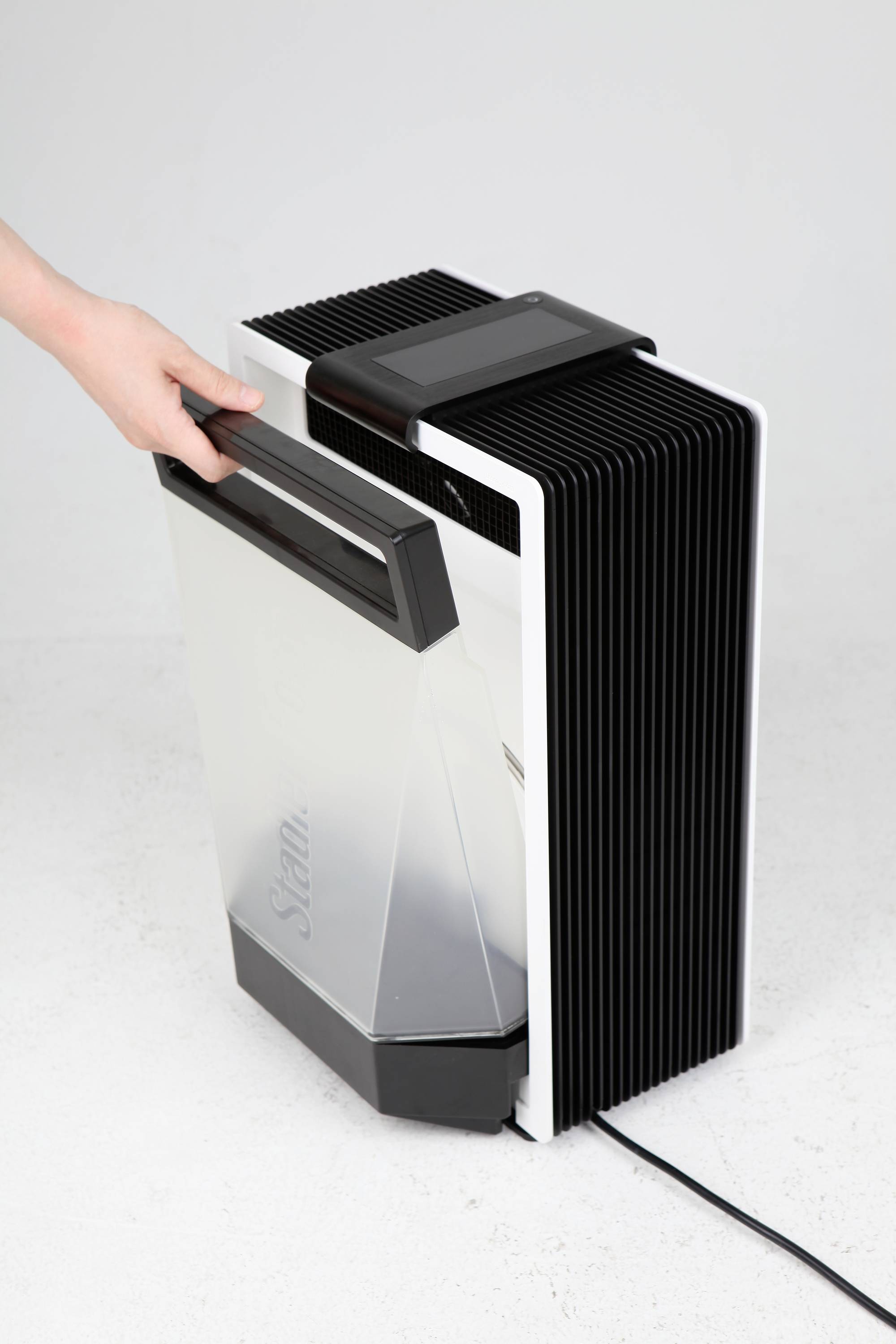 A hand operates a dehumidifier by pulling out the water tank. The device has a modern, black and white design.