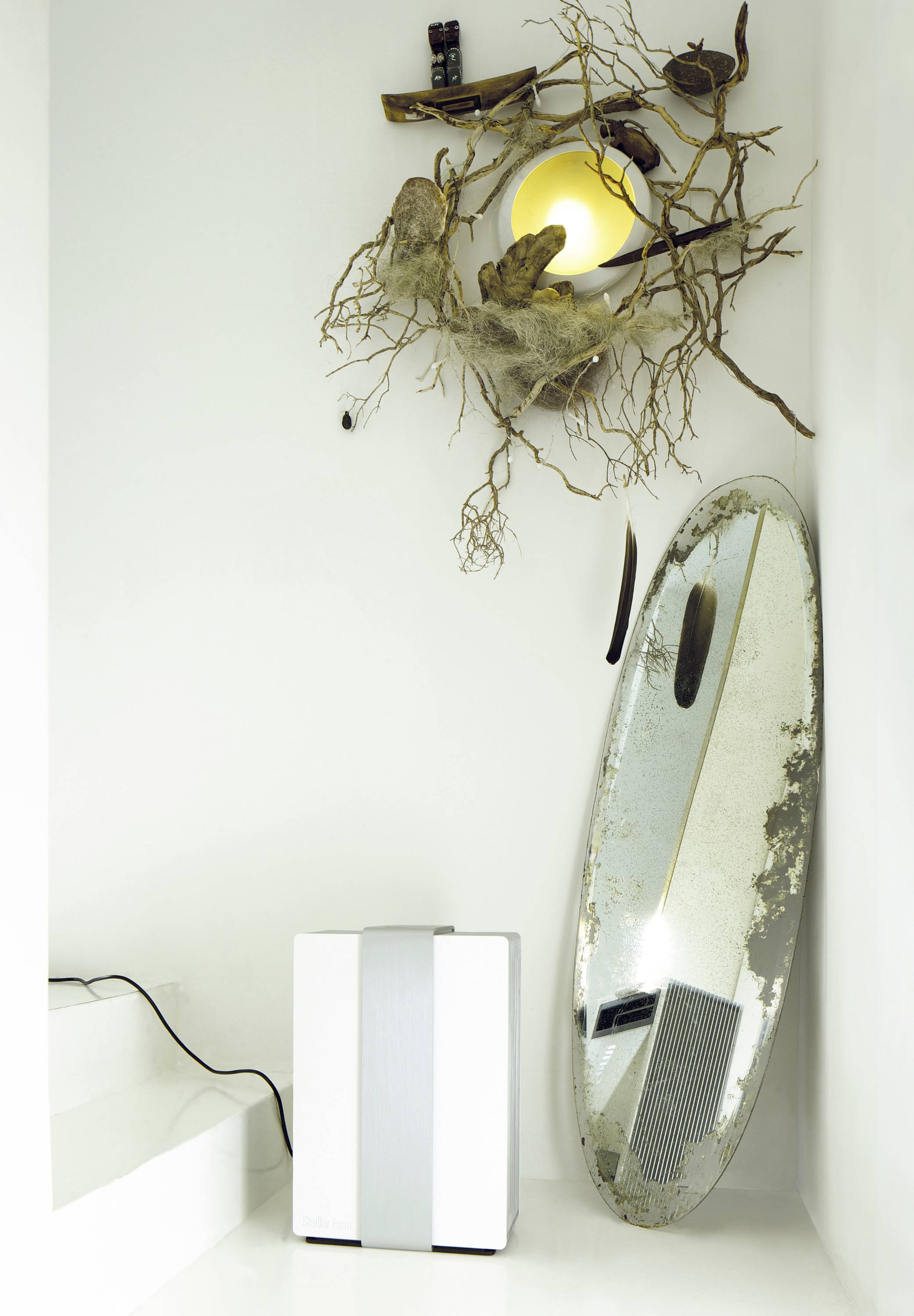 A decorative wall mirror with a rustic frame made of branches and another oval mirror beside it, on a white floor.