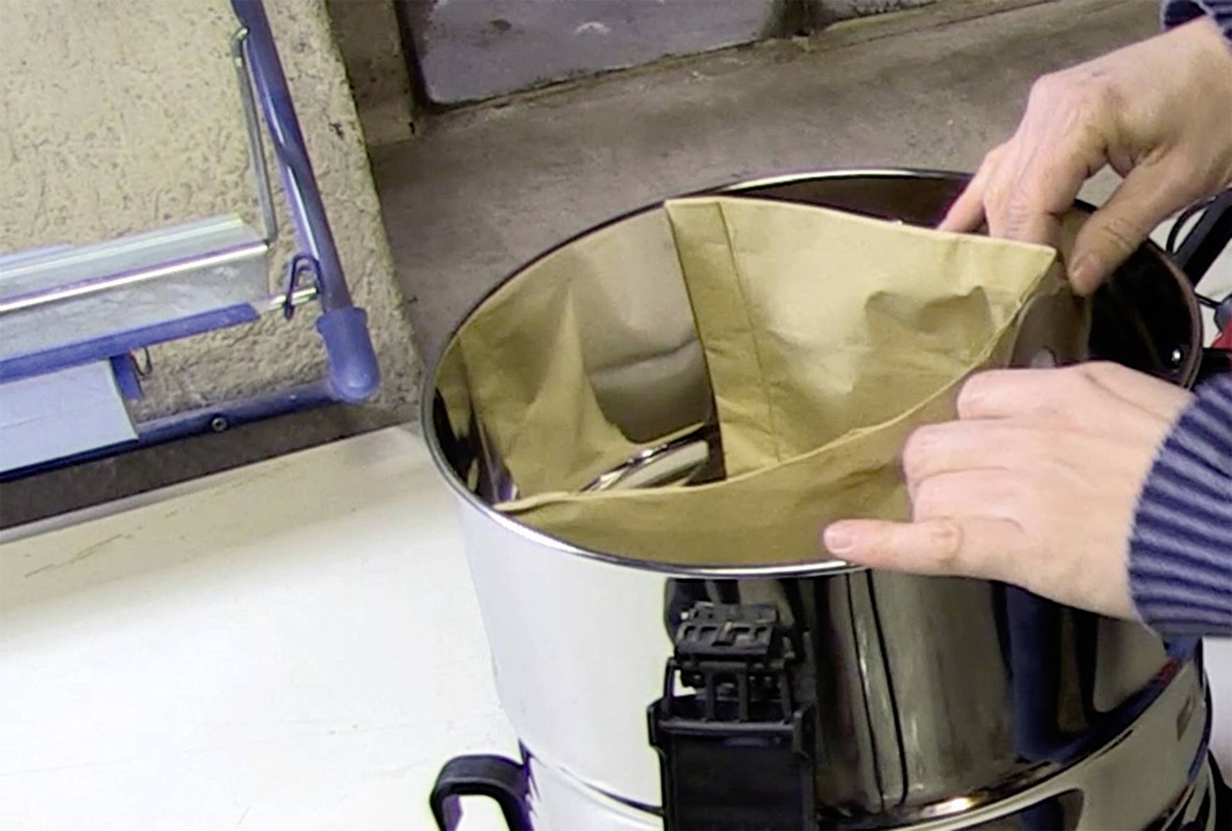 A person is placing a brown paper filter into a large, shiny metal container, presumably in preparation for a coffee machine.
