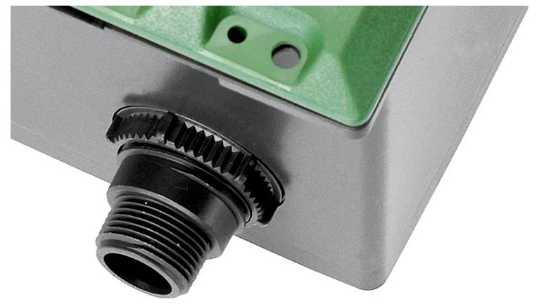 A close-up view of a plastic box corner with a black cable gland attached, used for securing and sealing cables in electronic enclosures.