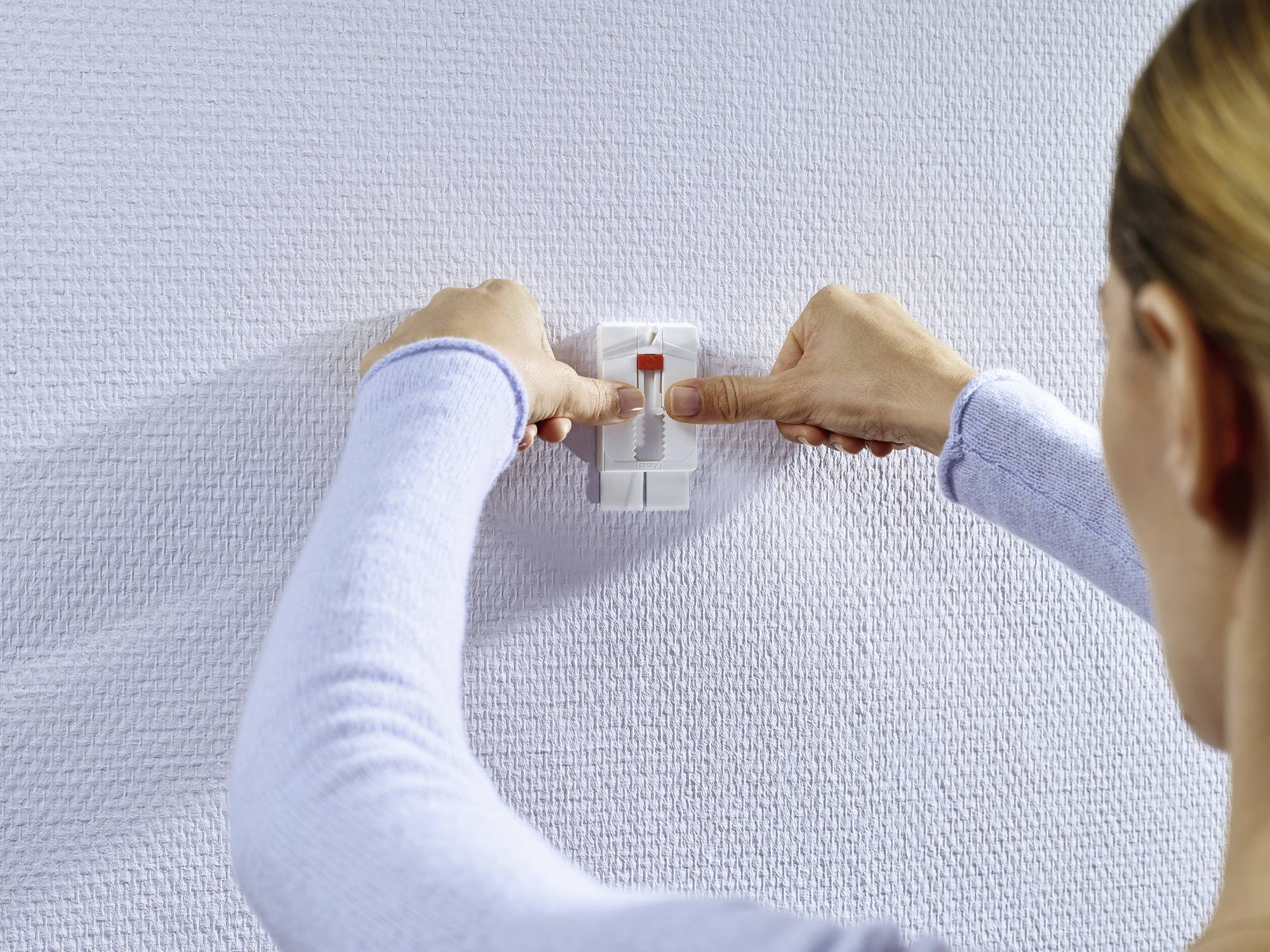A person is attaching a picture hanging strip to a textured wall. The strip is being aligned centrally.