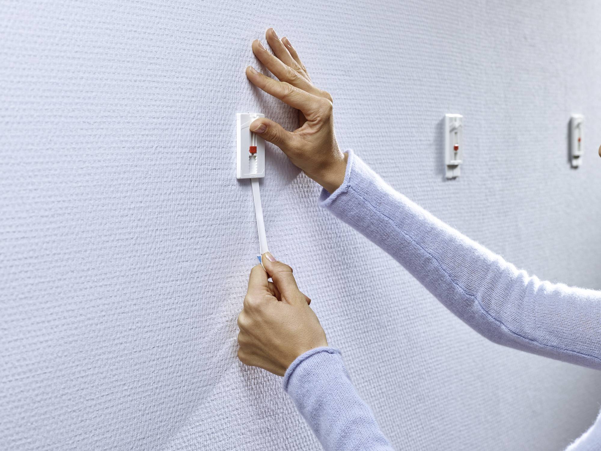 A hand pulls a cord light switch on a white wall. The switch is rectangular and attached to a textured surface.