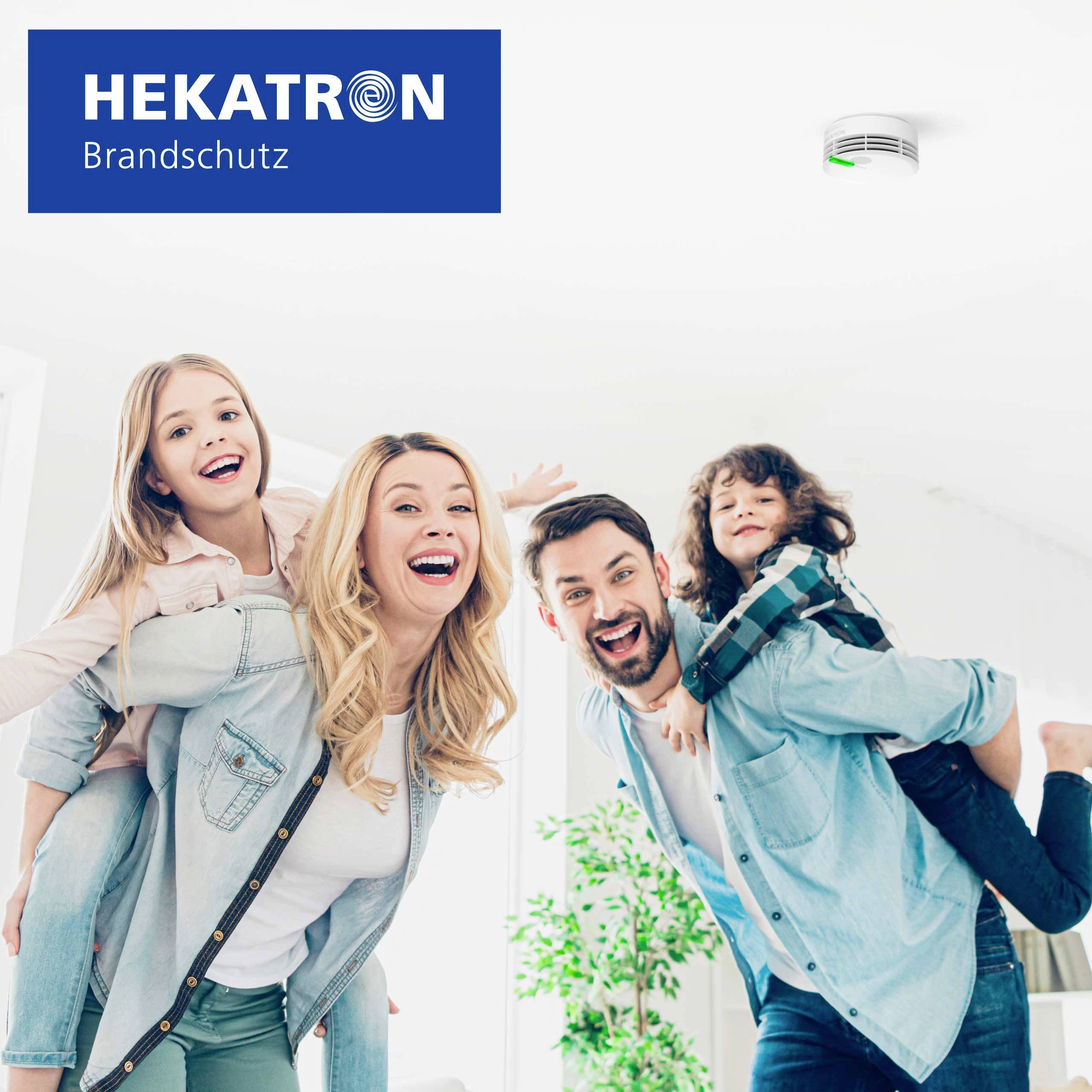 A family of four happily poses in a bright room with a smoke detector on the ceiling, promoting Hekatron Brandschutz products.