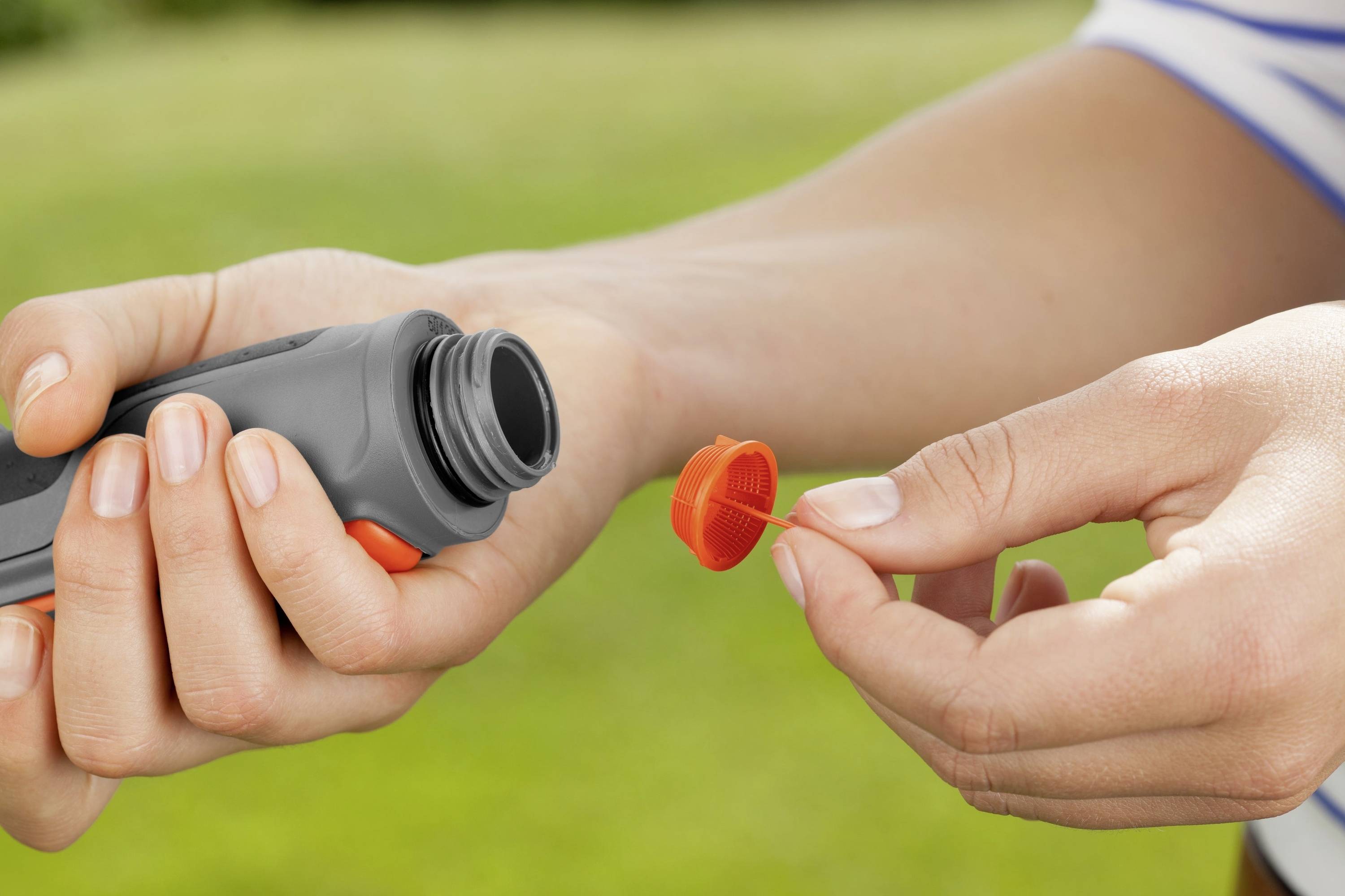 A person is holding a small open plastic bottle in one hand and the red lid in the other hand, against a blurred green background.